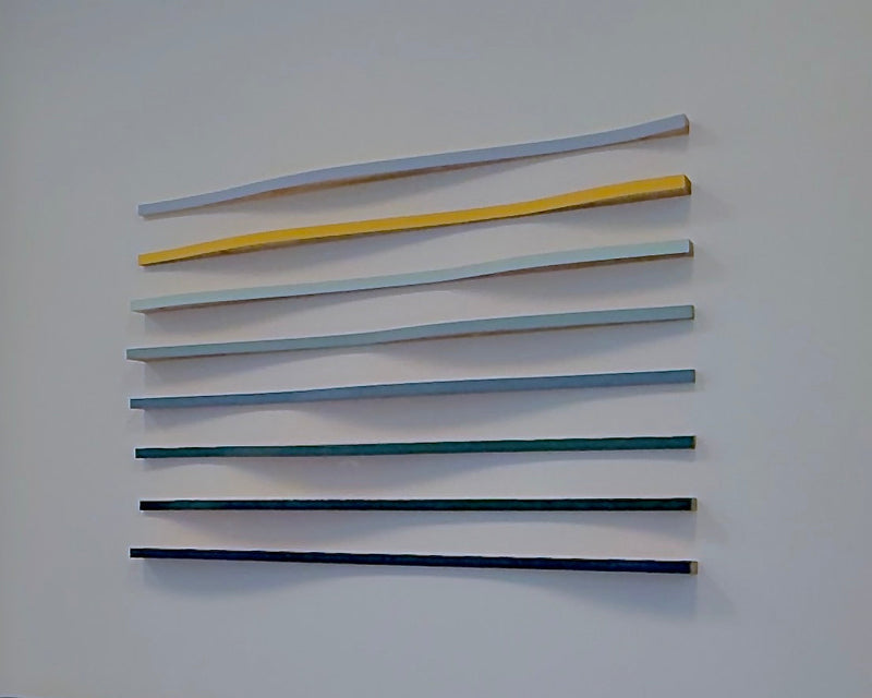 A set of seven curved wooden wall shelves in varying colors (from light blue to dark navy) mounted on a white wall above a light blue sofa.