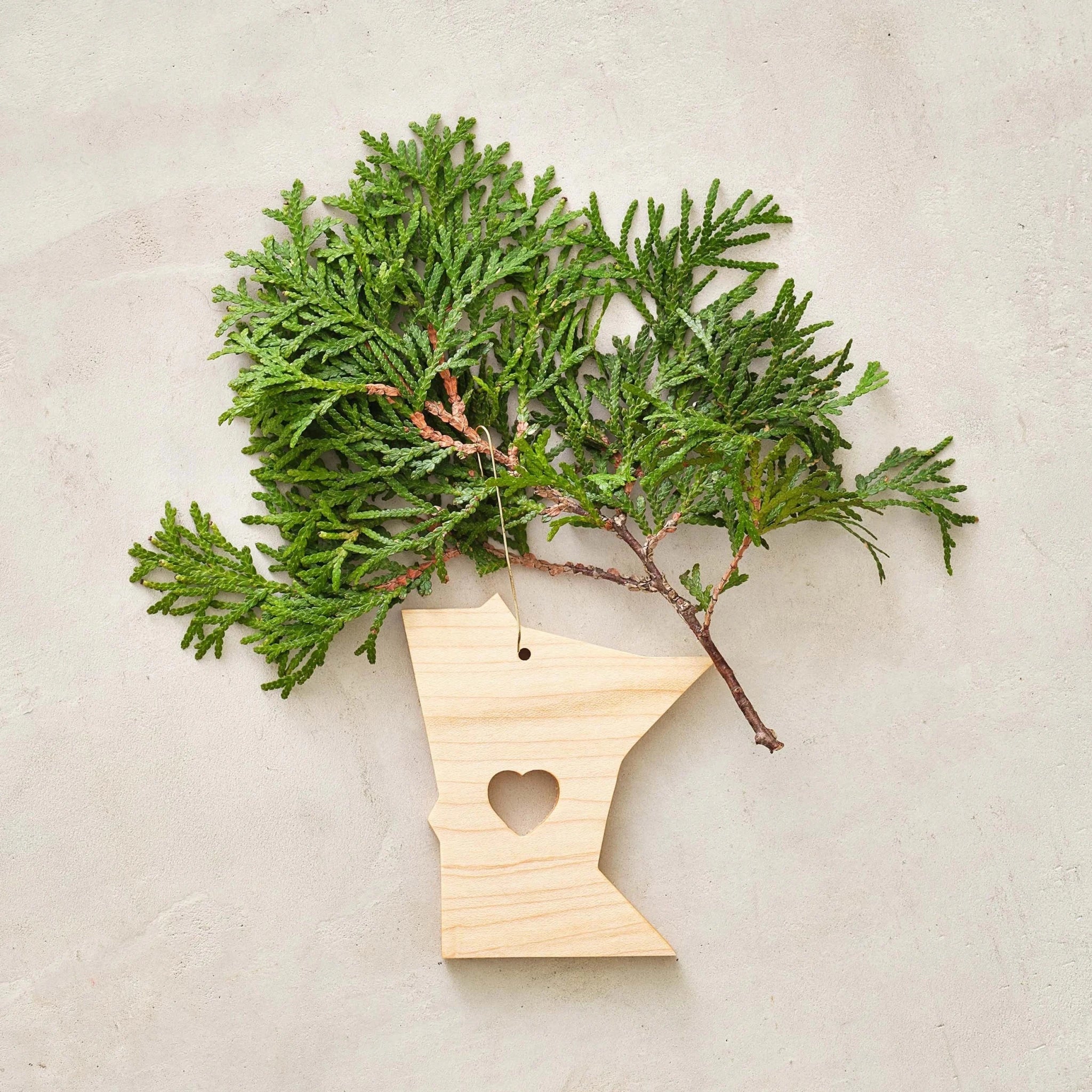 Light maple Minnesota ornament with heart cutout beneath green cedar sprig