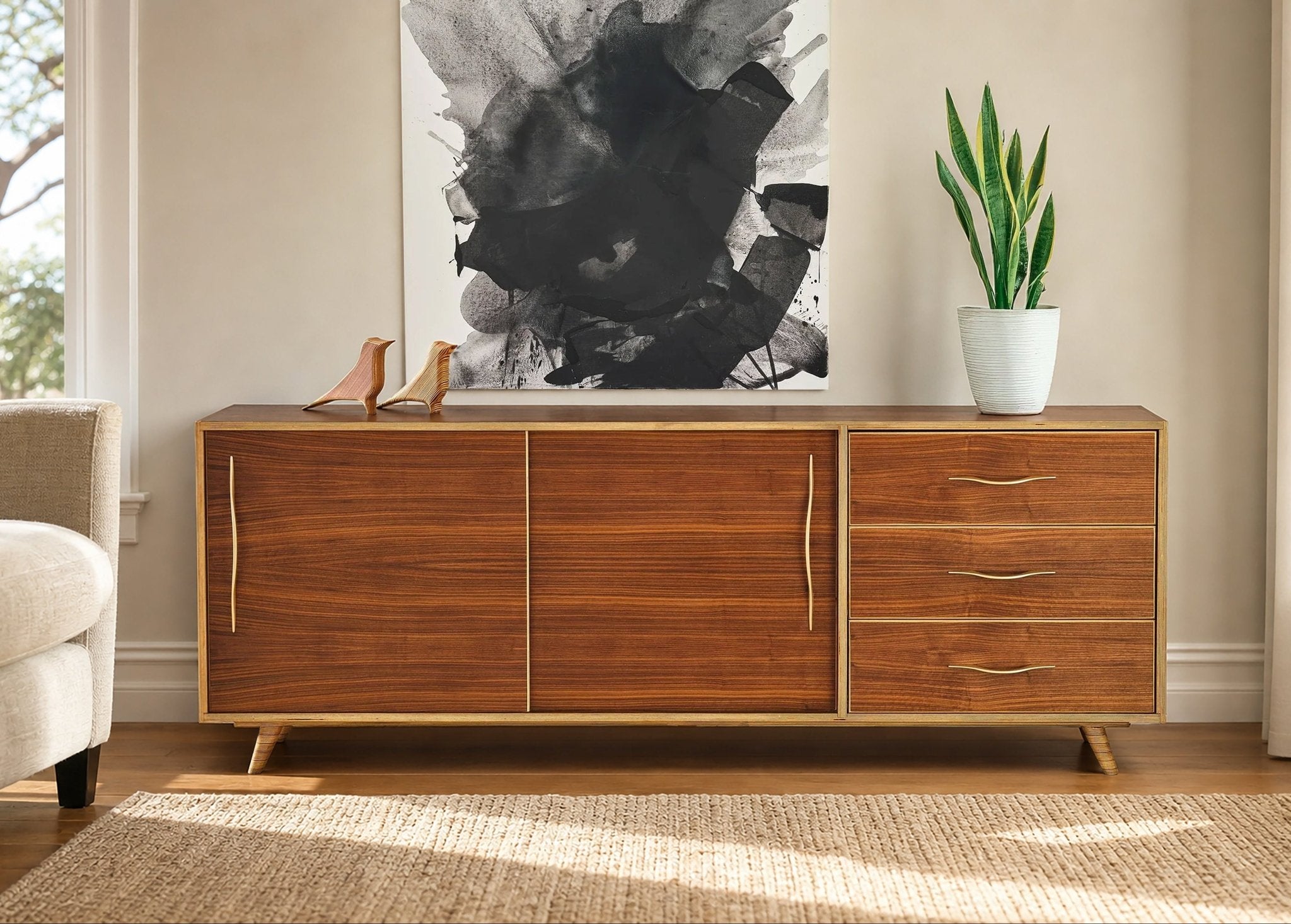 Mid-century modern wood sideboard with walnut finish, featuring cabinet doors and drawers with brass pulls in a bright room.