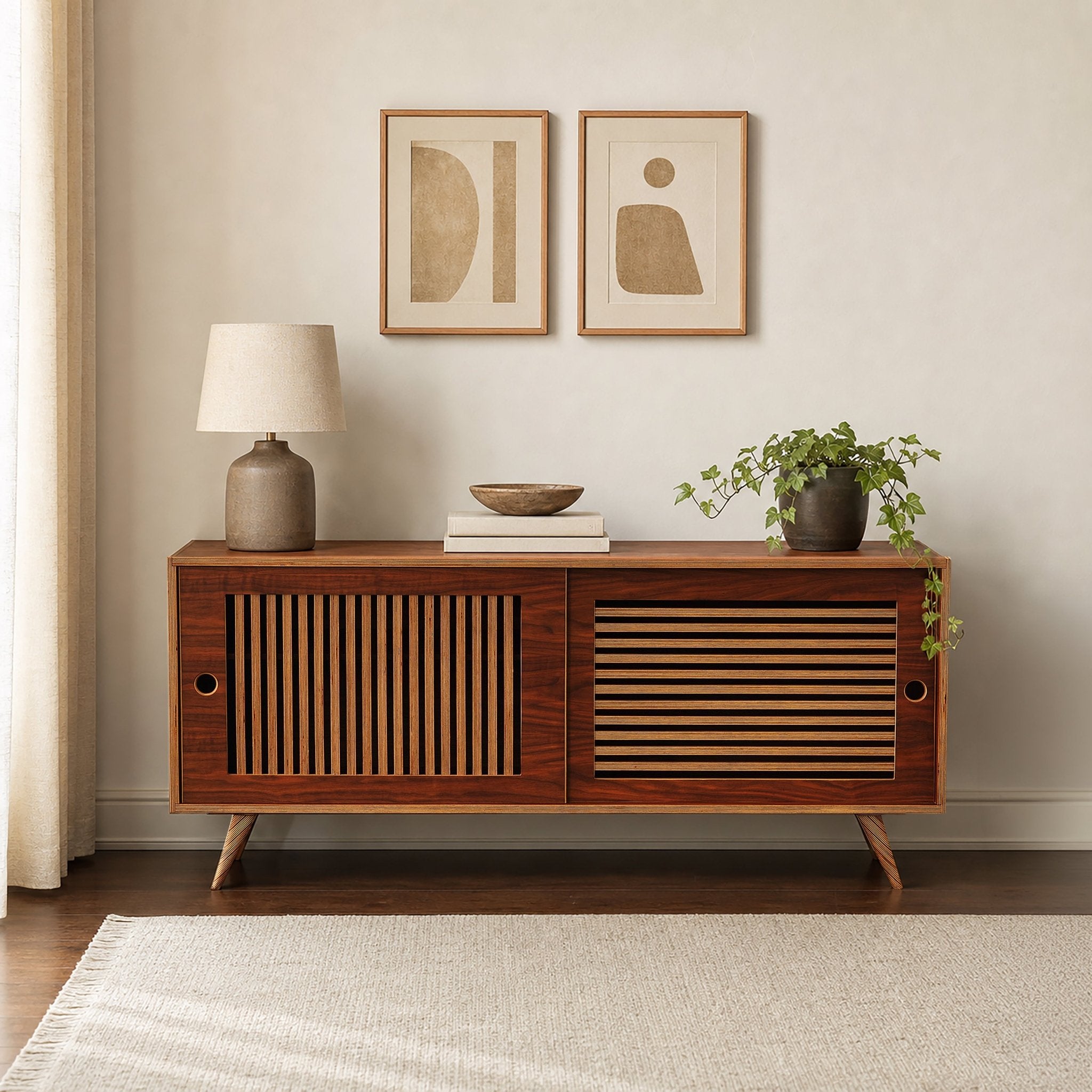 A mid-century modern media console in a walnut finish, styled in a minimalist room with  lamp, books, bowl, and plant on top.