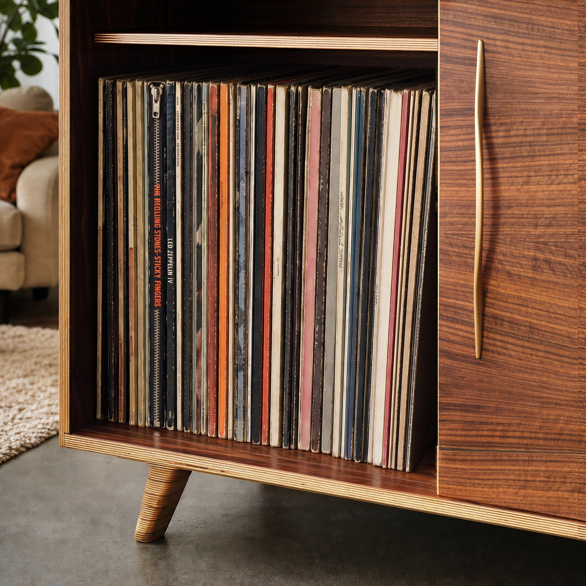 Close-up of mid-century modern wooden record cabinet with a brass handle, filled with vinyl records, in a living room.