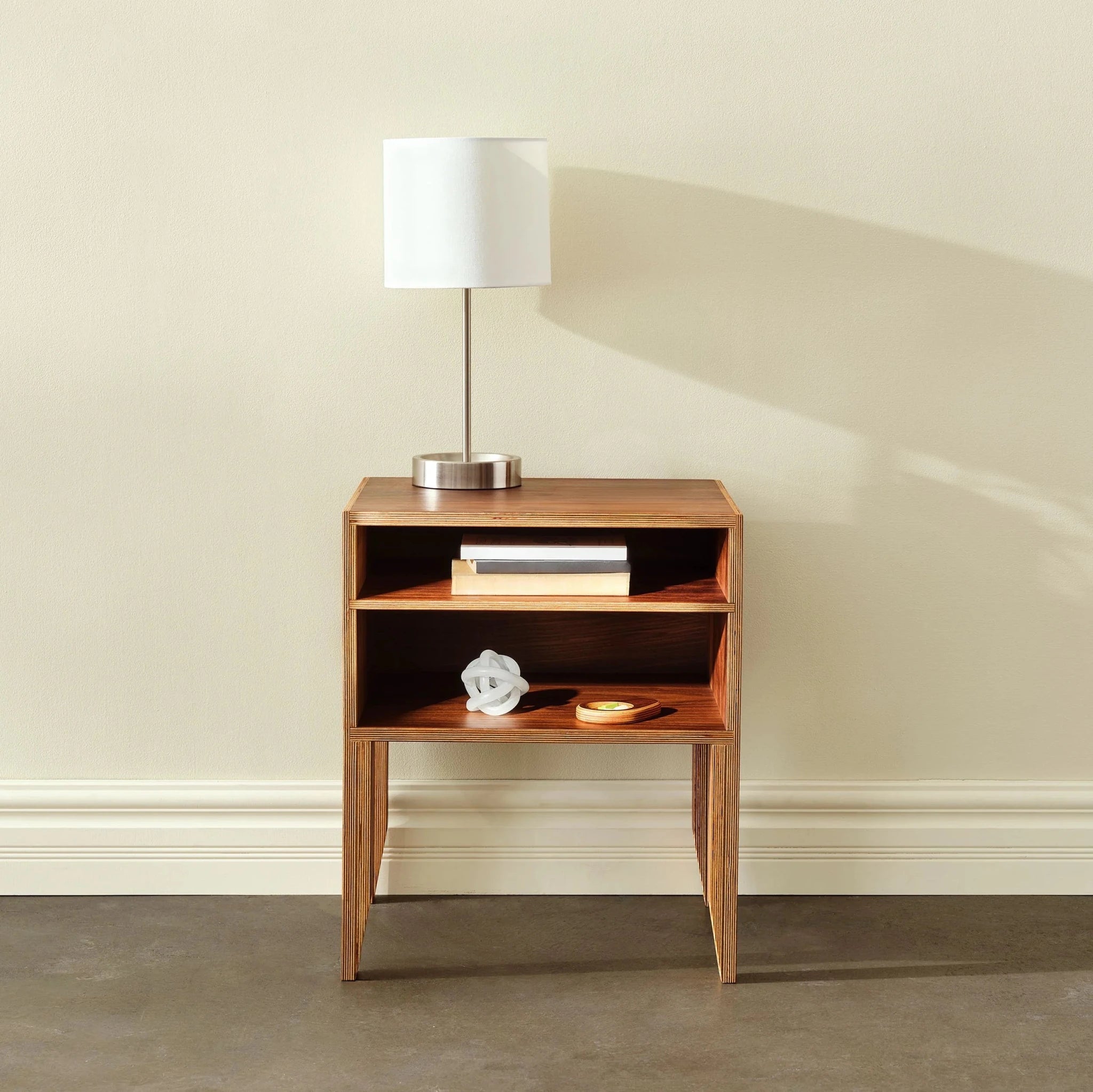 Front view of walnut open-shelf nightstand with table lamp, books and knot sculpture