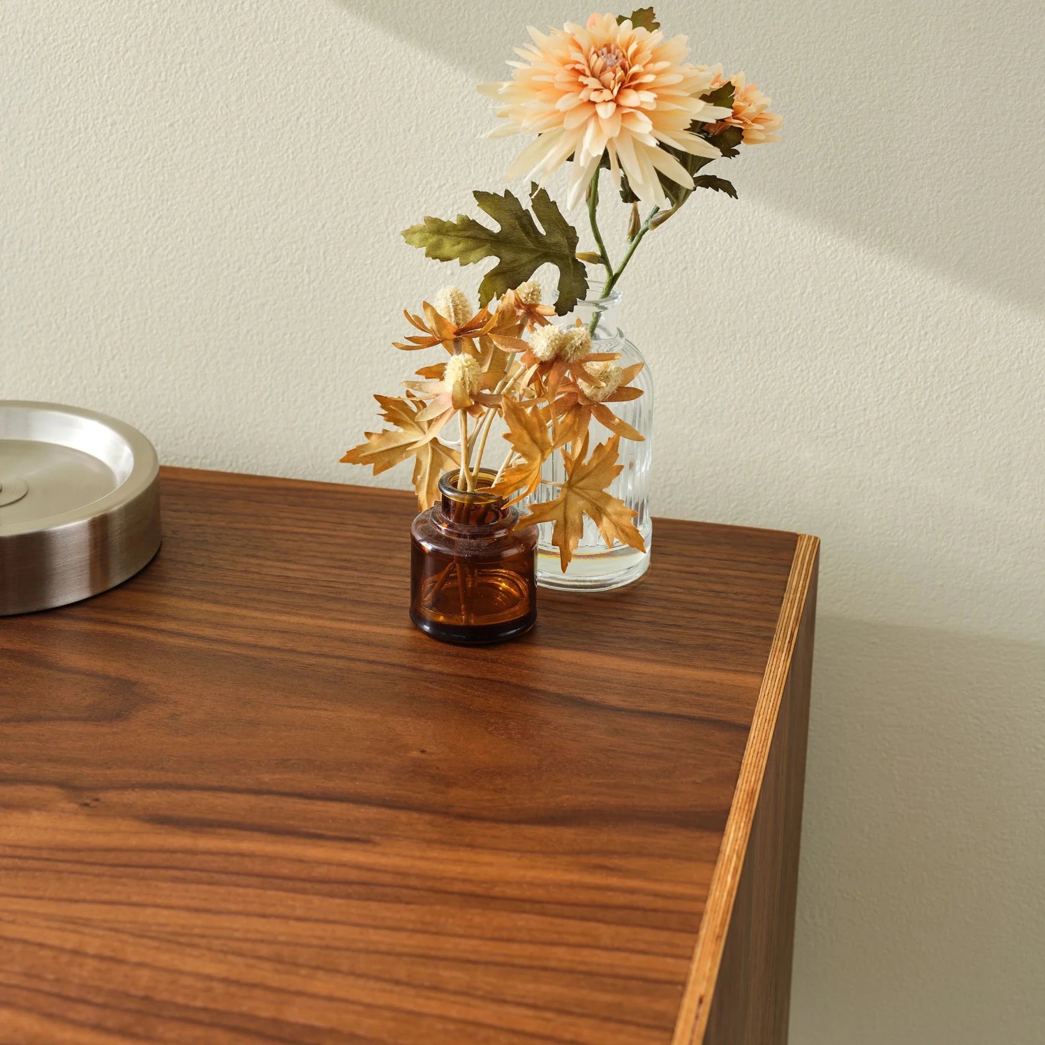 Walnut nightstand top detail with amber bud vase, dried flowers and metal dish