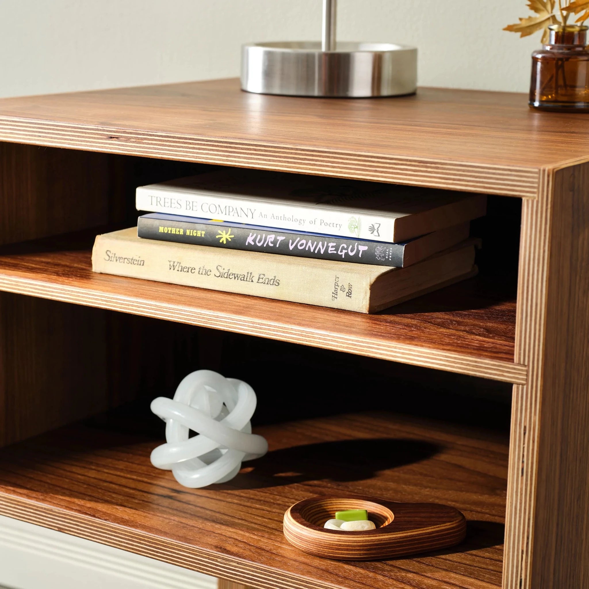 Detail of walnut open-shelf nightstand with stacked books, white knot sculpture and tray