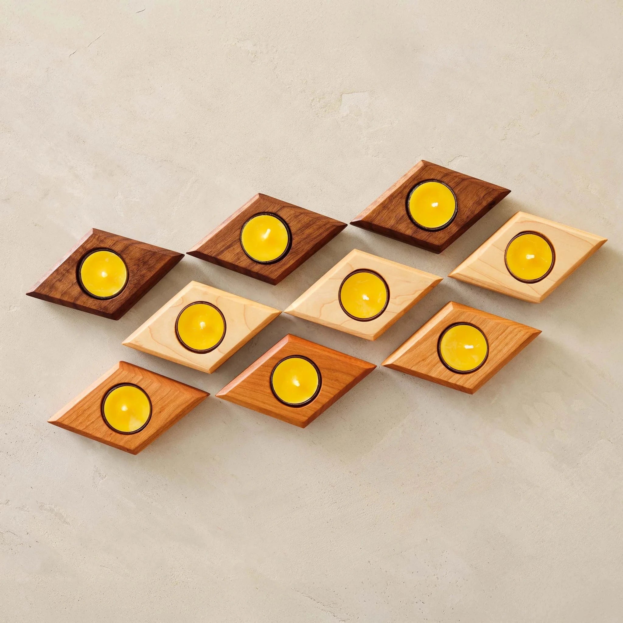 Nine diamond-shaped tealight holders in walnut, cherry, maple with yellow candles, overhead view