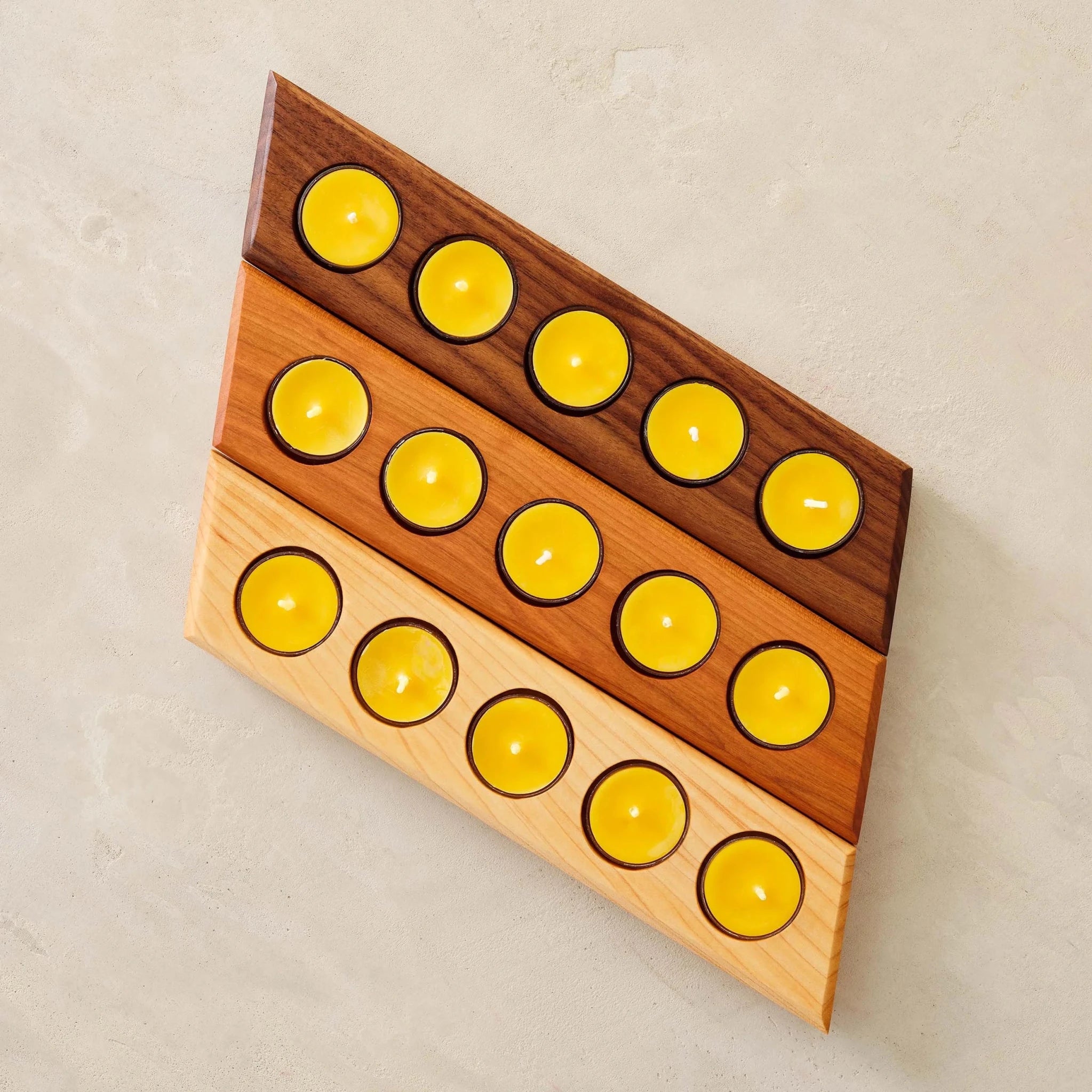Three stacked wood tealight bars in walnut, cherry, maple filled with yellow candles, overhead