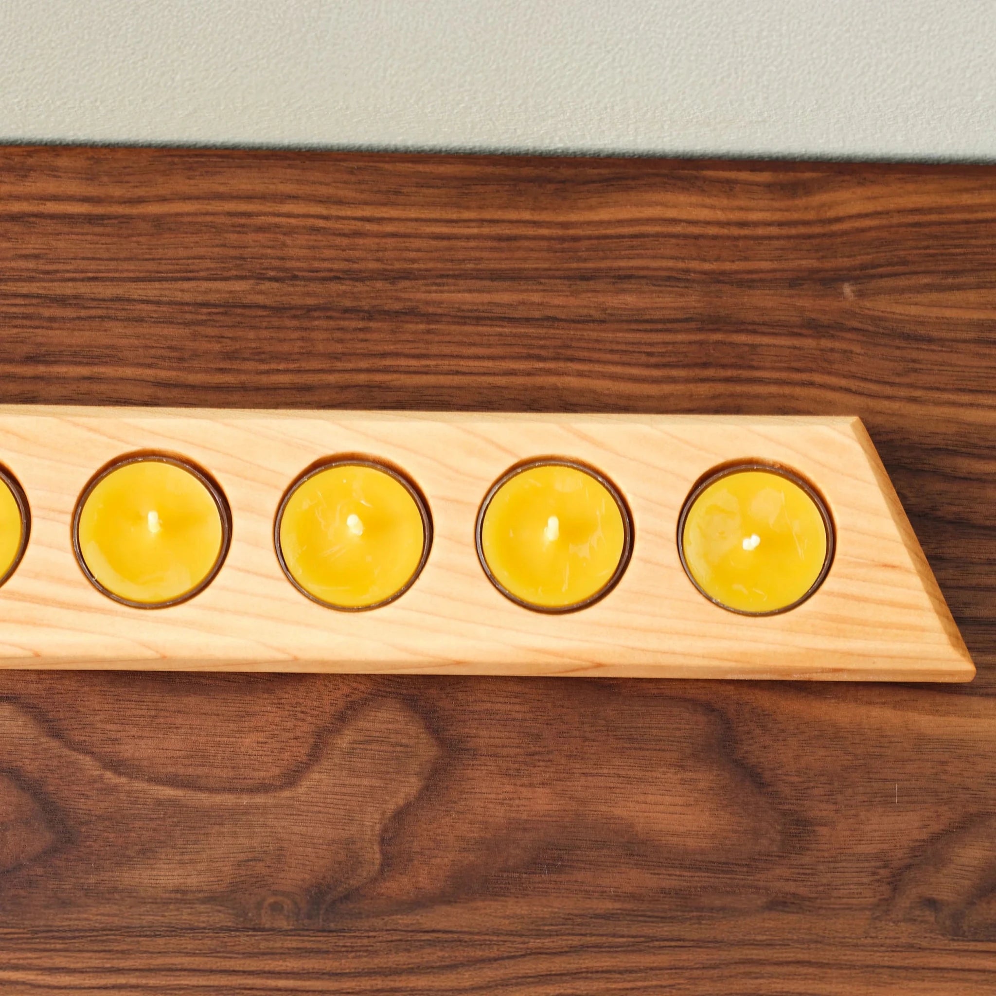 Closeup of maple tealight bar holding five yellow candles on walnut surface