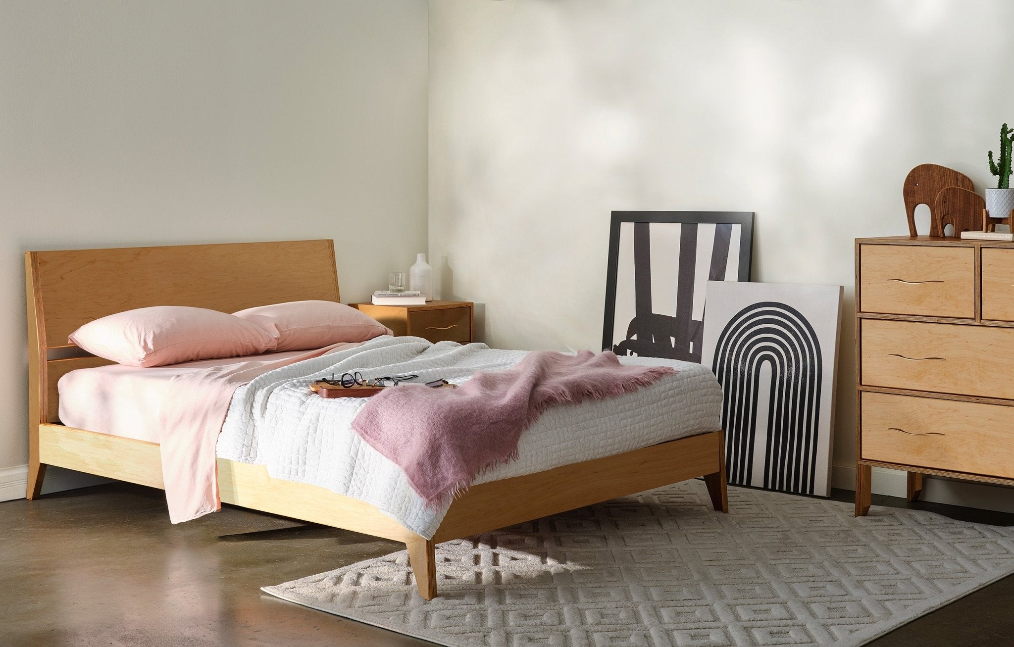 Maple platform bed with pink bedding, matching dresser, artwork and patterned rug