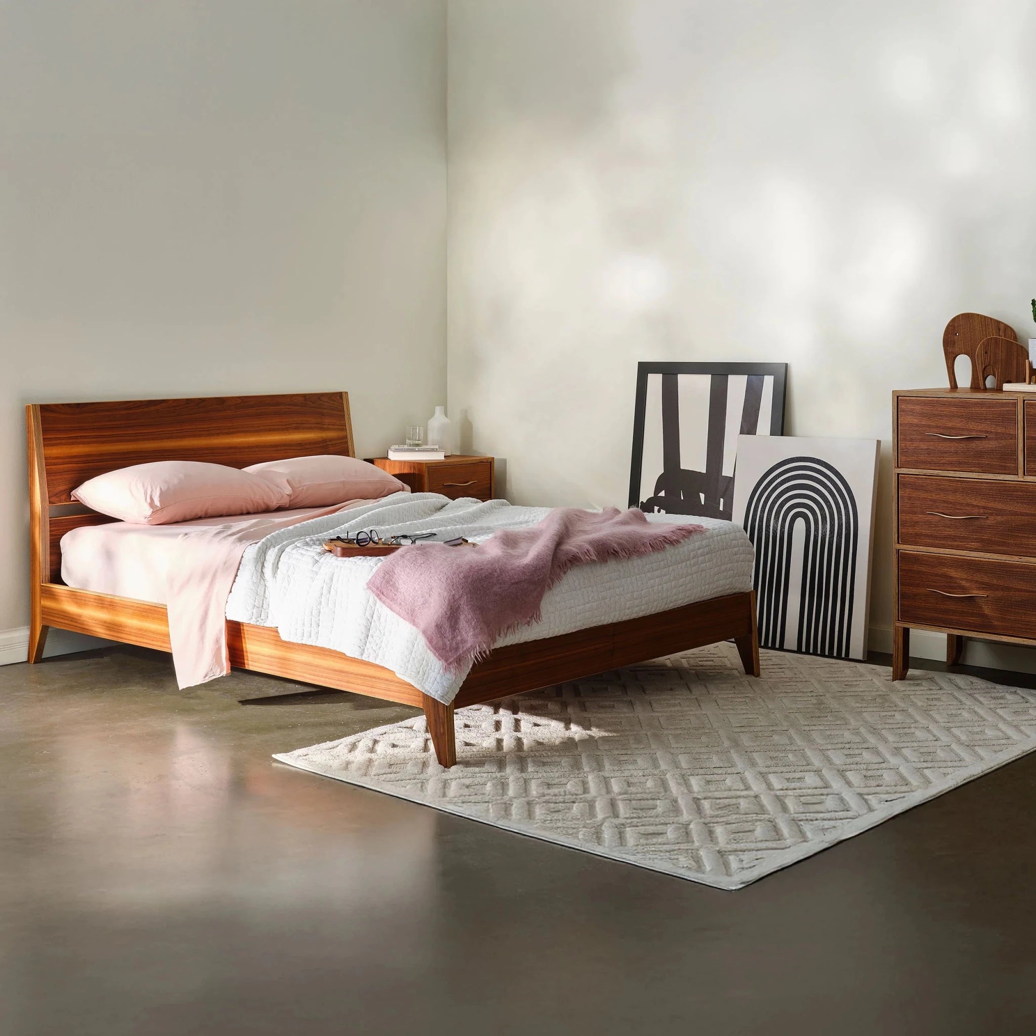Bedroom with walnut platform bed, pink bedding and matching dresser, framed artwork