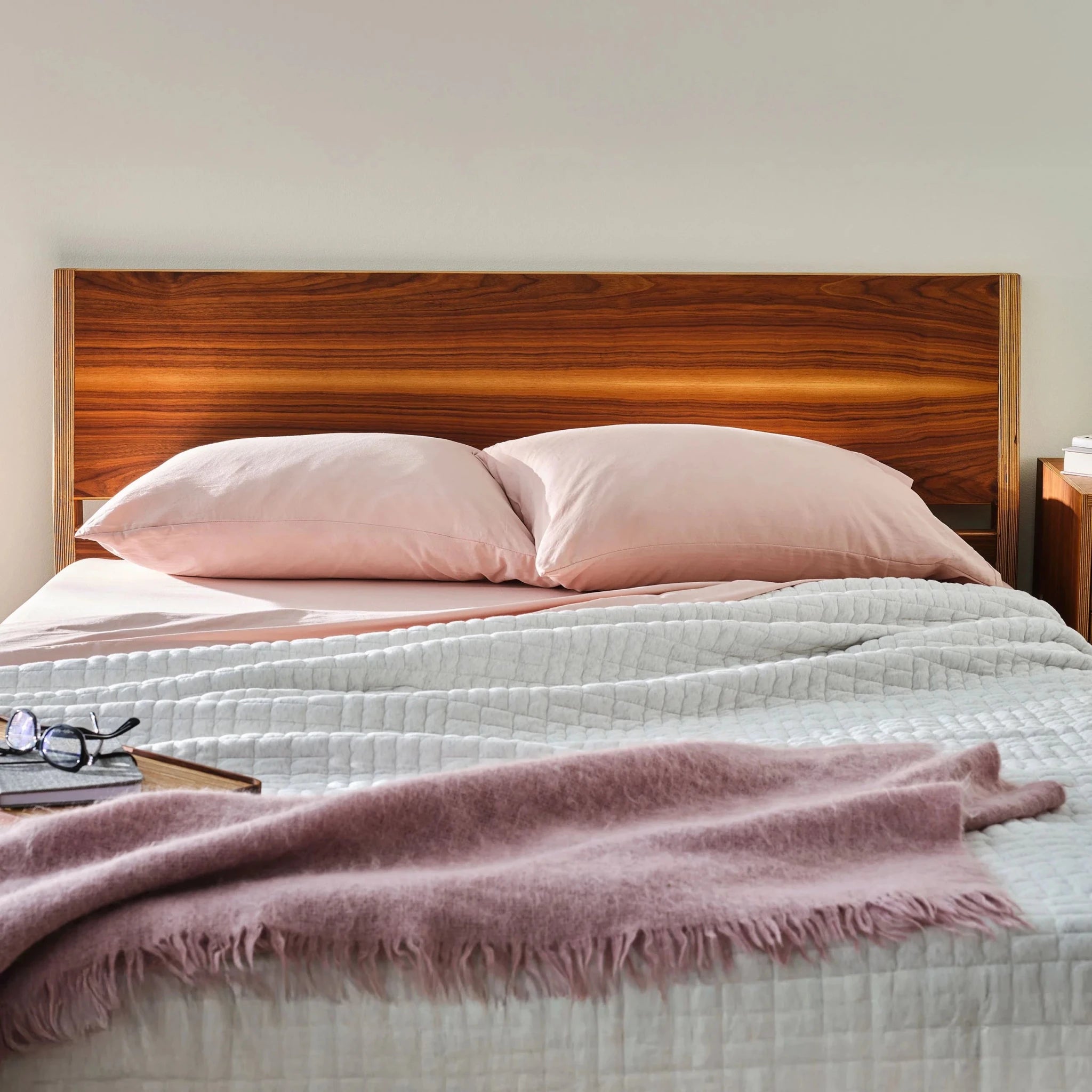 Walnut platform bed headboard close-up with pink pillows, gray quilt, purple throw