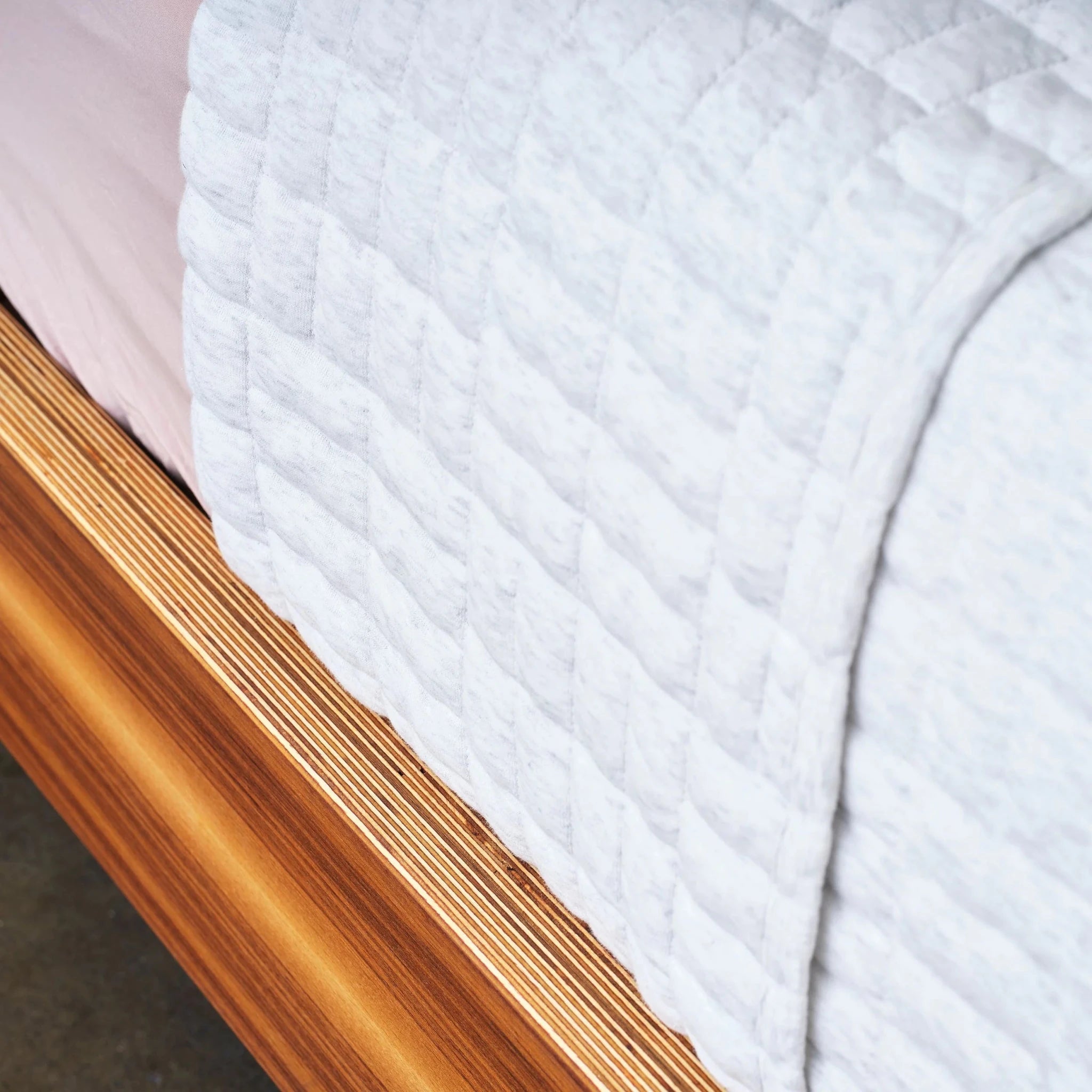 Close-up walnut platform bed side rail with layered birch edge and white quilt