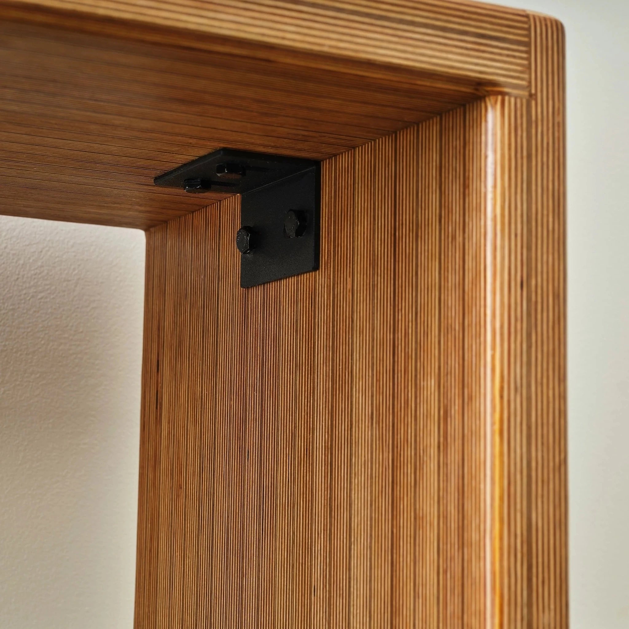 Closeup of black metal L-bracket joining layered Baltic birch entryway bench frame
