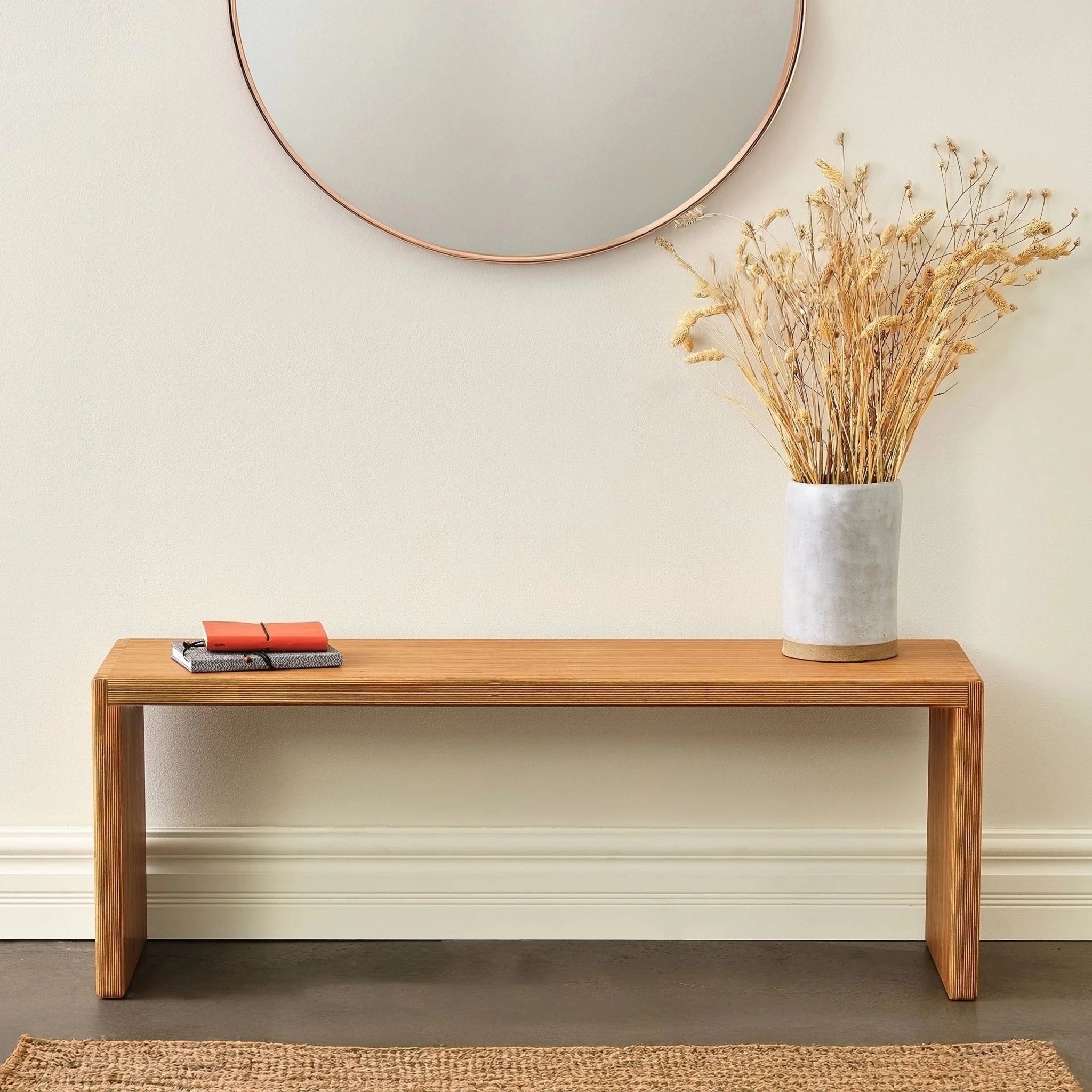Light Baltic birch bench styled with dried florals and notebooks, round mirror above
