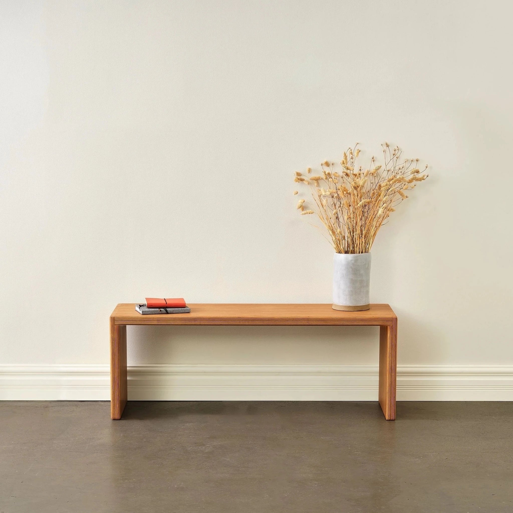 Baltic birch bench styled with dried floral vase and stacked notebooks against white wall