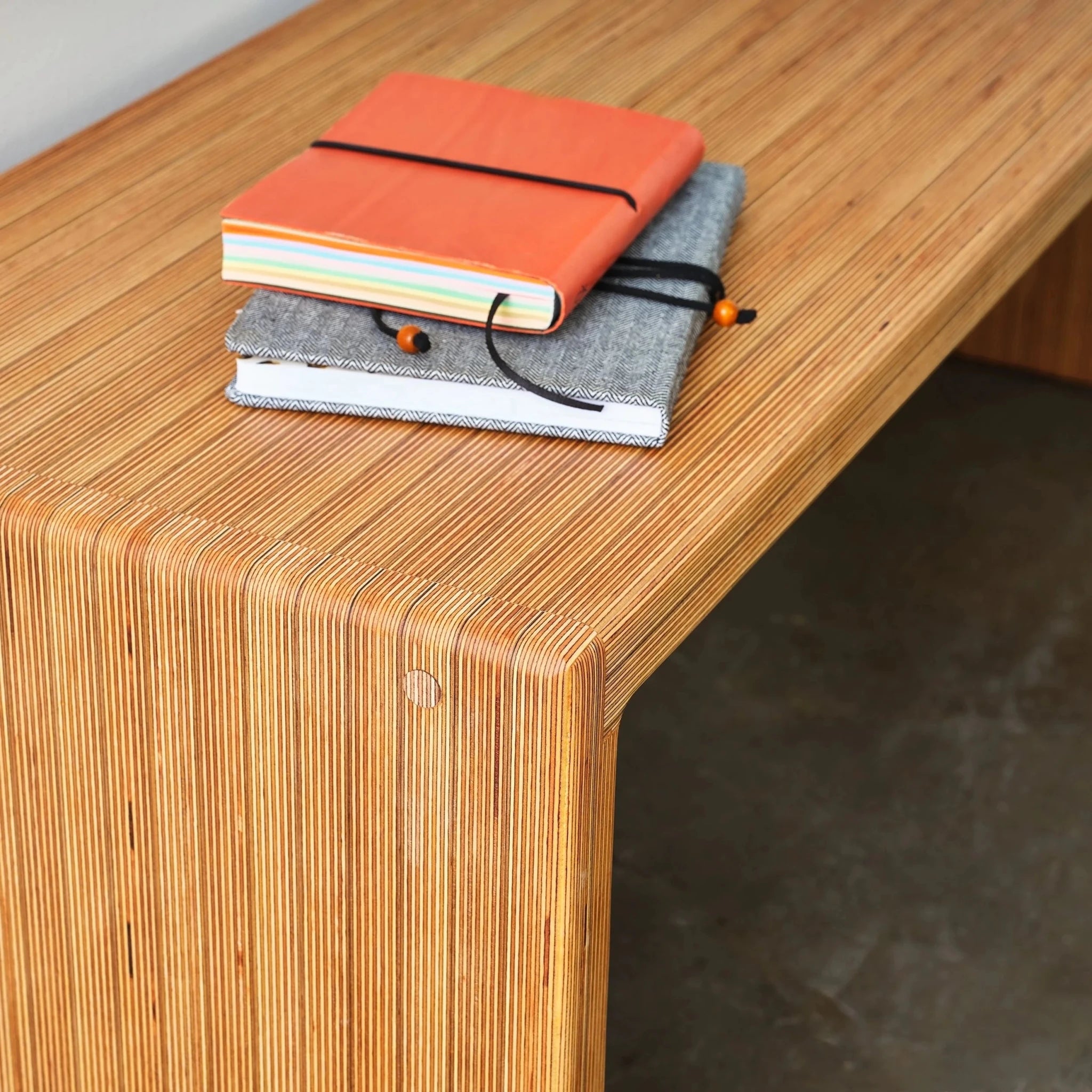 Angled close-up of Baltic birch bench corner, striped layered plywood edges, stacked notebooks