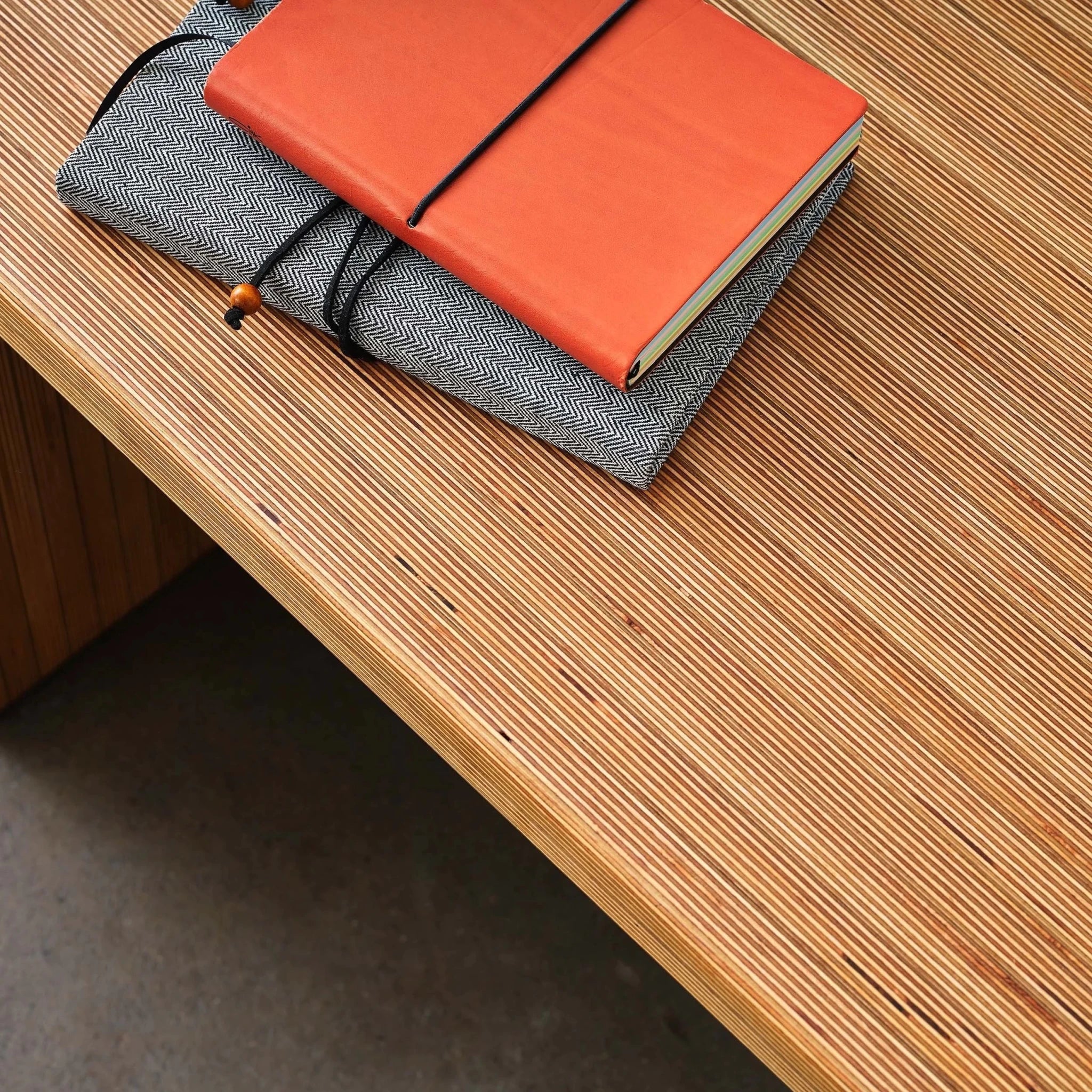 Layered Baltic birch bench top corner holding an orange leather and herringbone journal