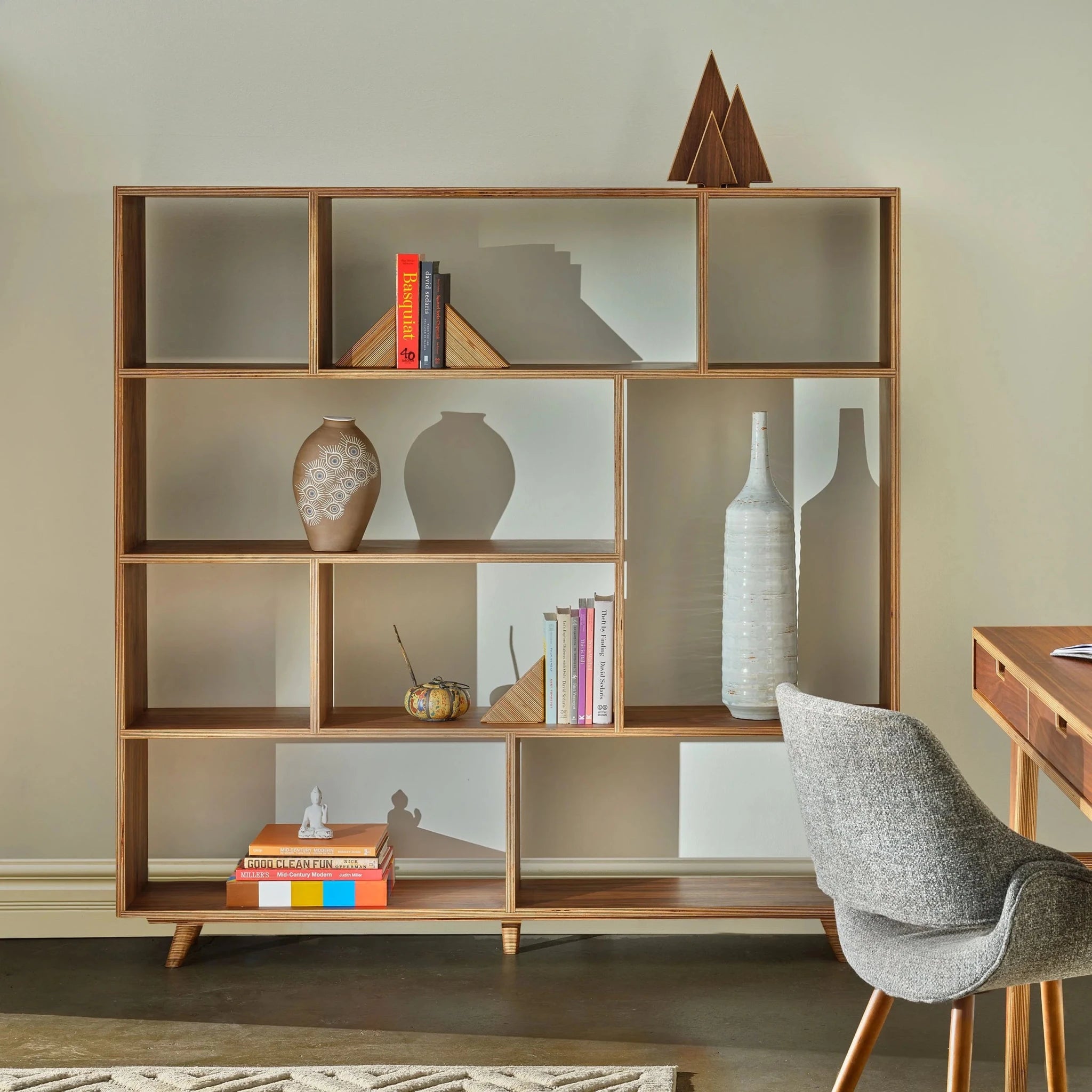 Styled walnut bookcase with staggered shelves holding books, vases, and decorative objects