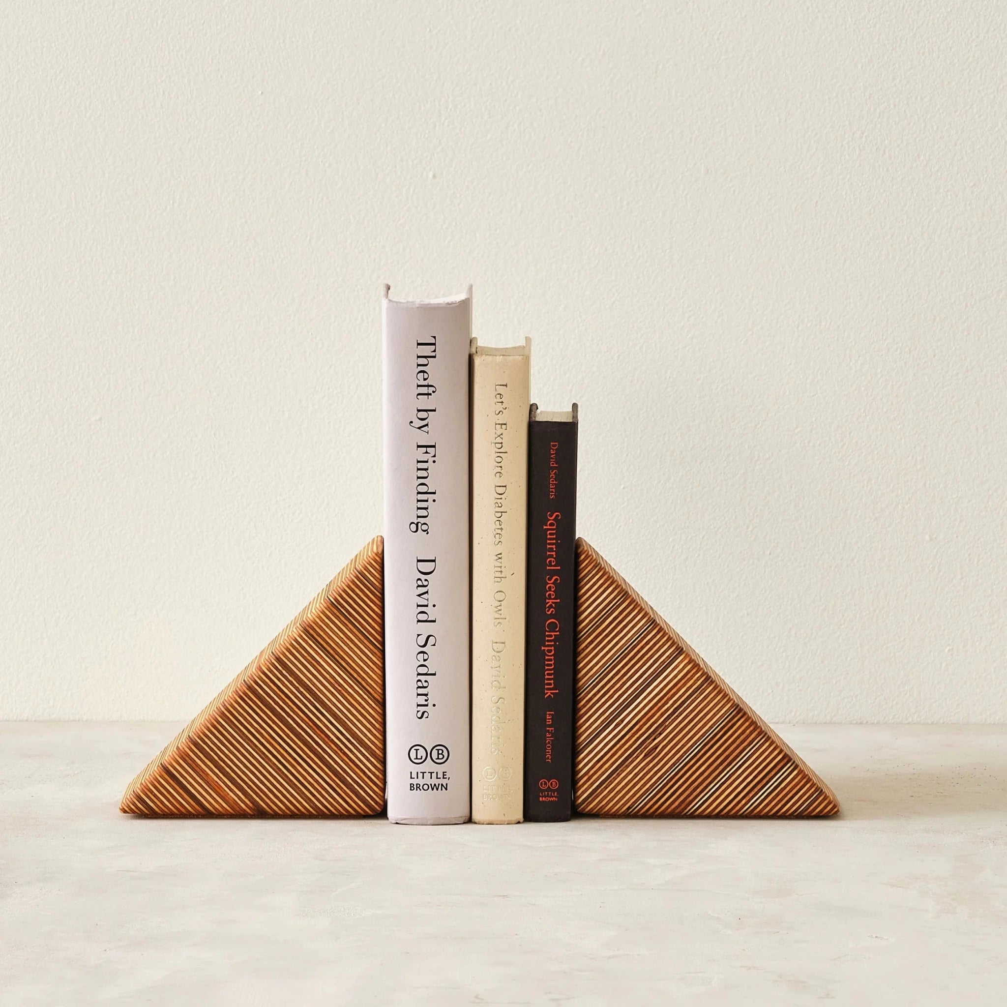 Layered birch wedge bookends holding three upright books, striped edge grain forward