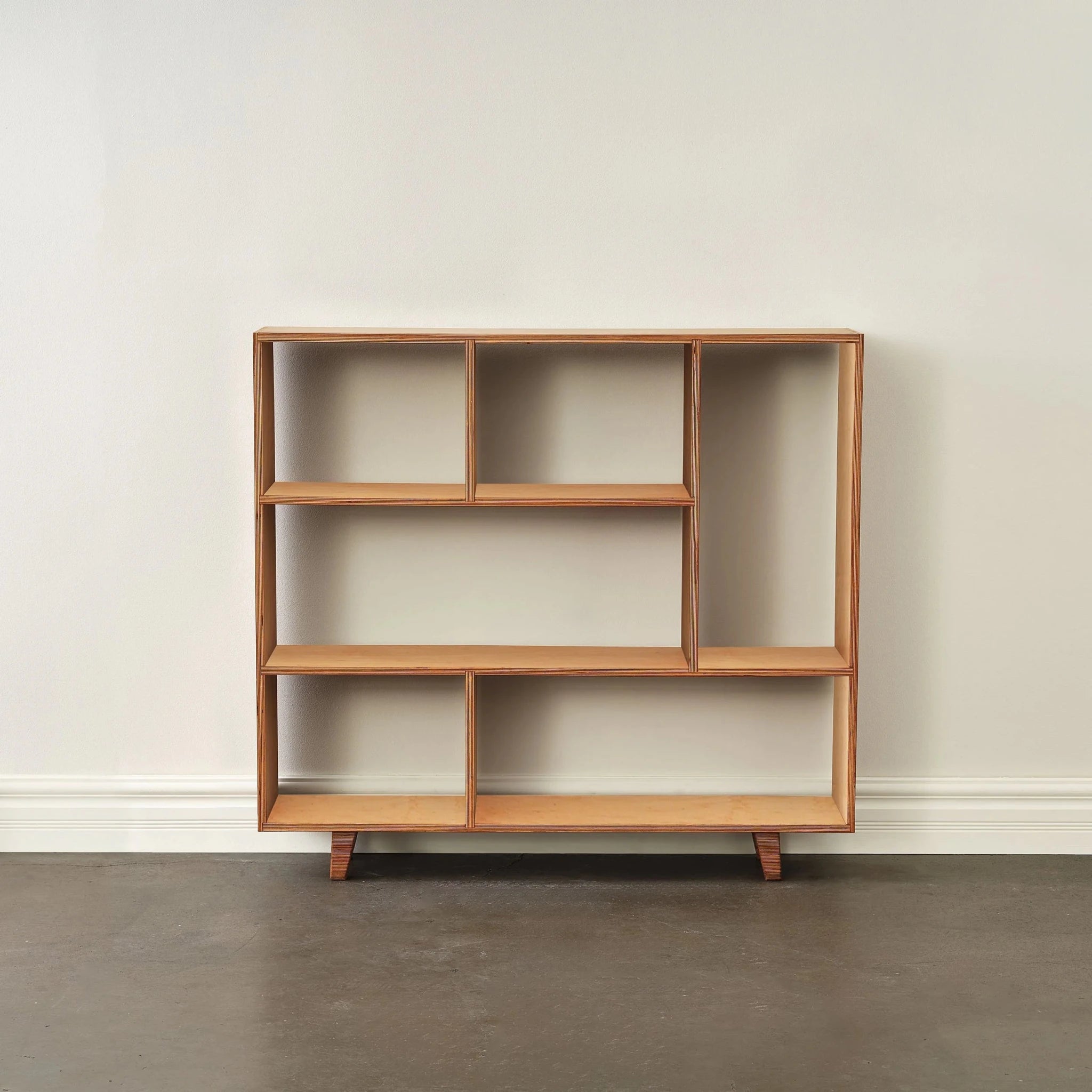 Empty maple bookcase with asymmetric staggered shelves, front view, light birch tone