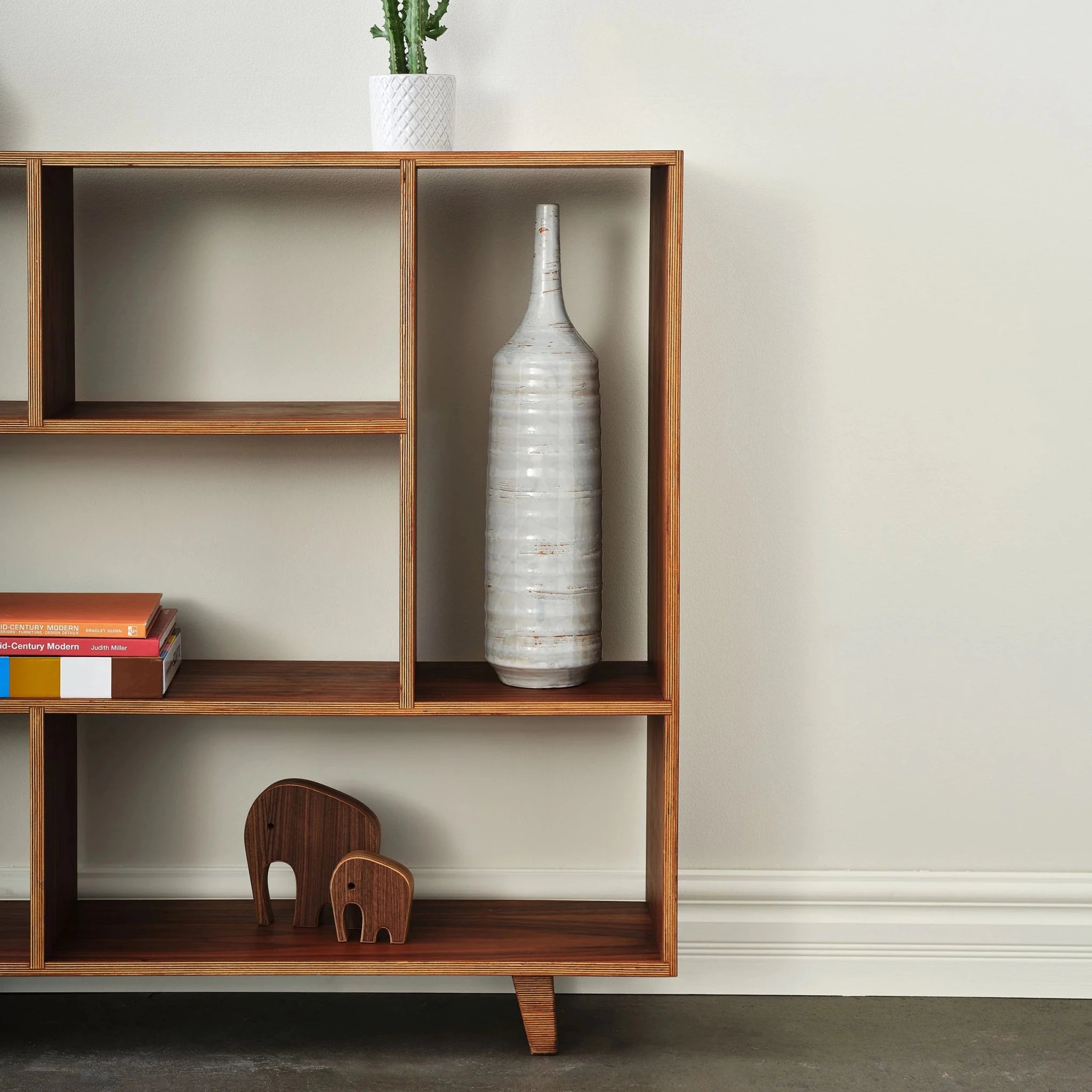 Walnut and birch plywood bookcase with cactus, white vase, books, carved elephant figurines