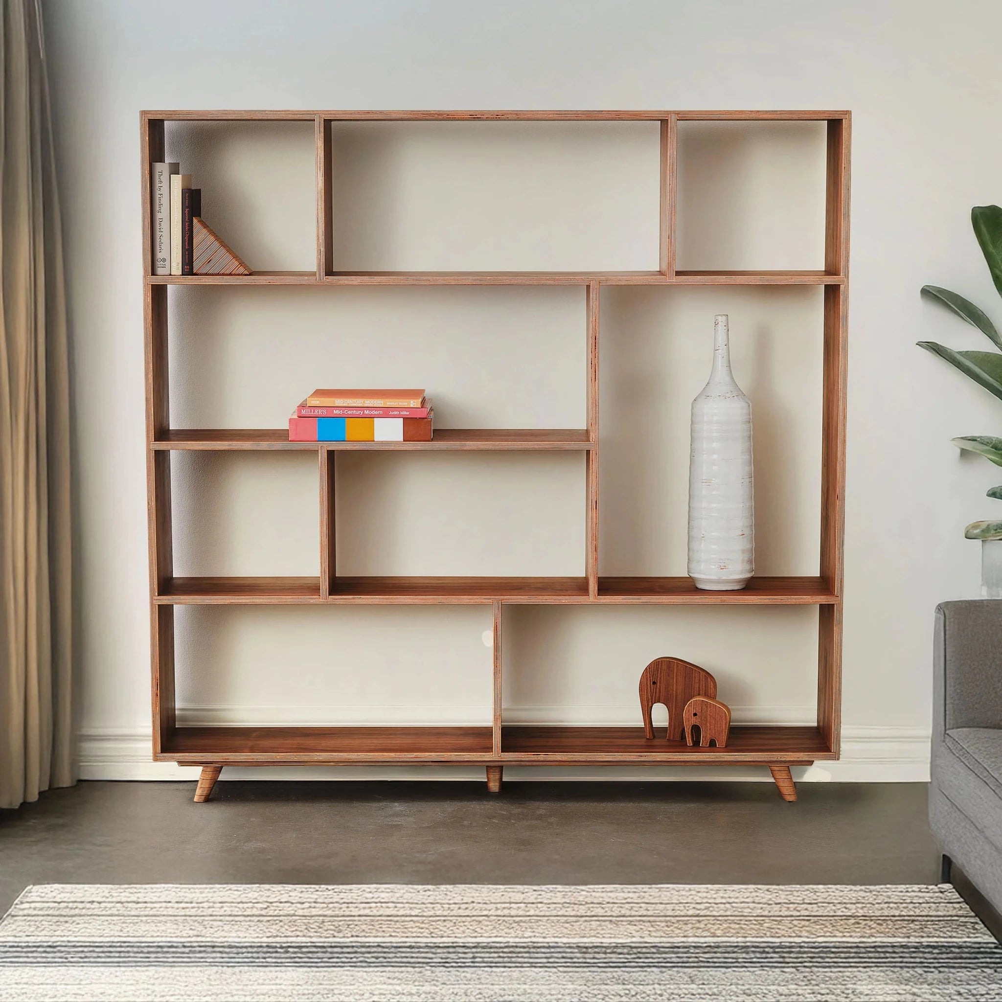 Styled walnut bookcase in living room with white vase, books, elephants, rug