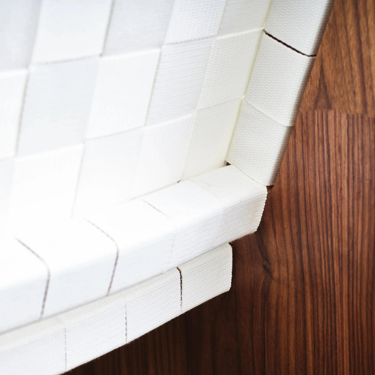 Closeup of white woven webbing wrapping around walnut frame at chair back corner