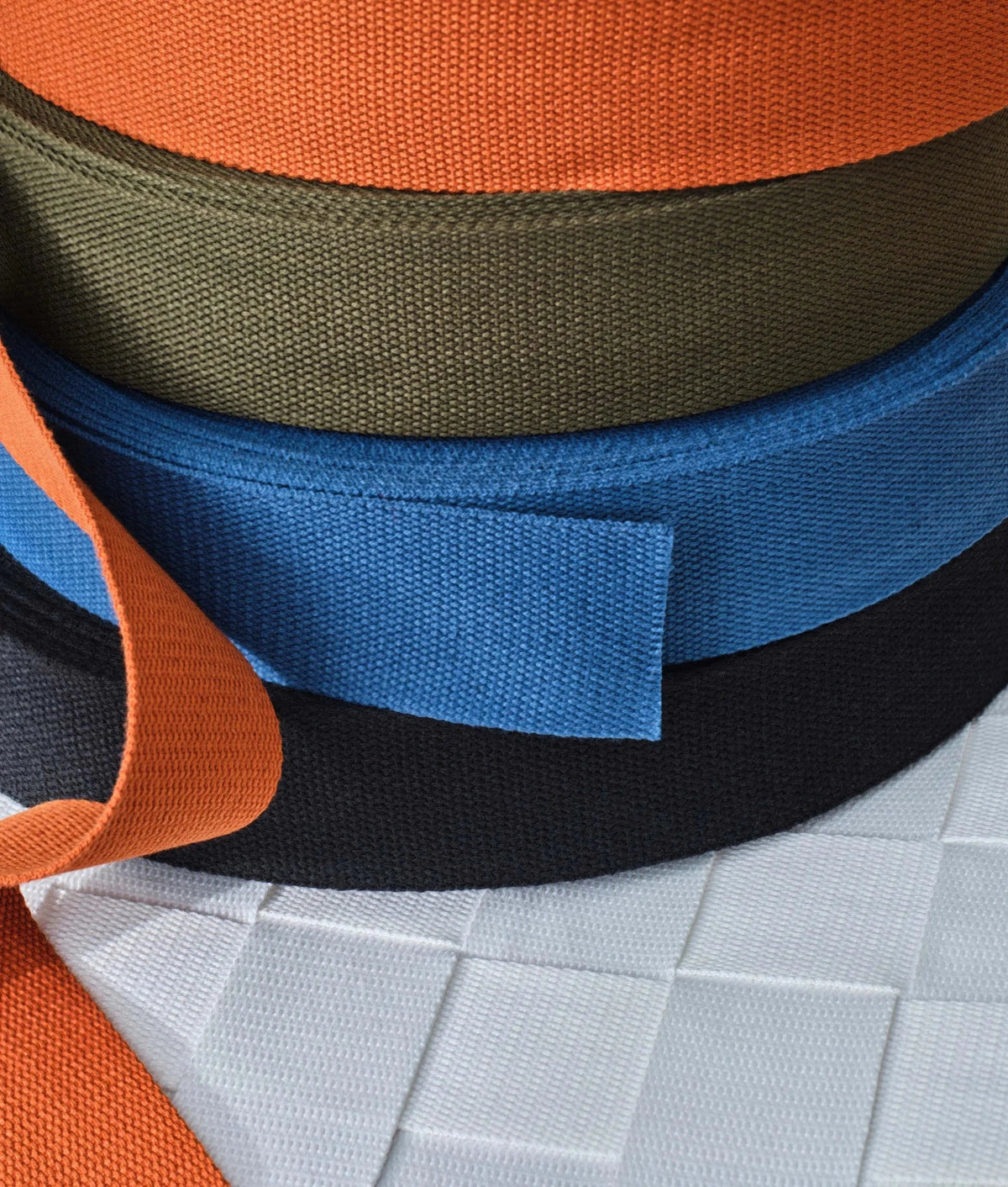Rolls of webbing strap color options: orange, olive, blue, black over white seat