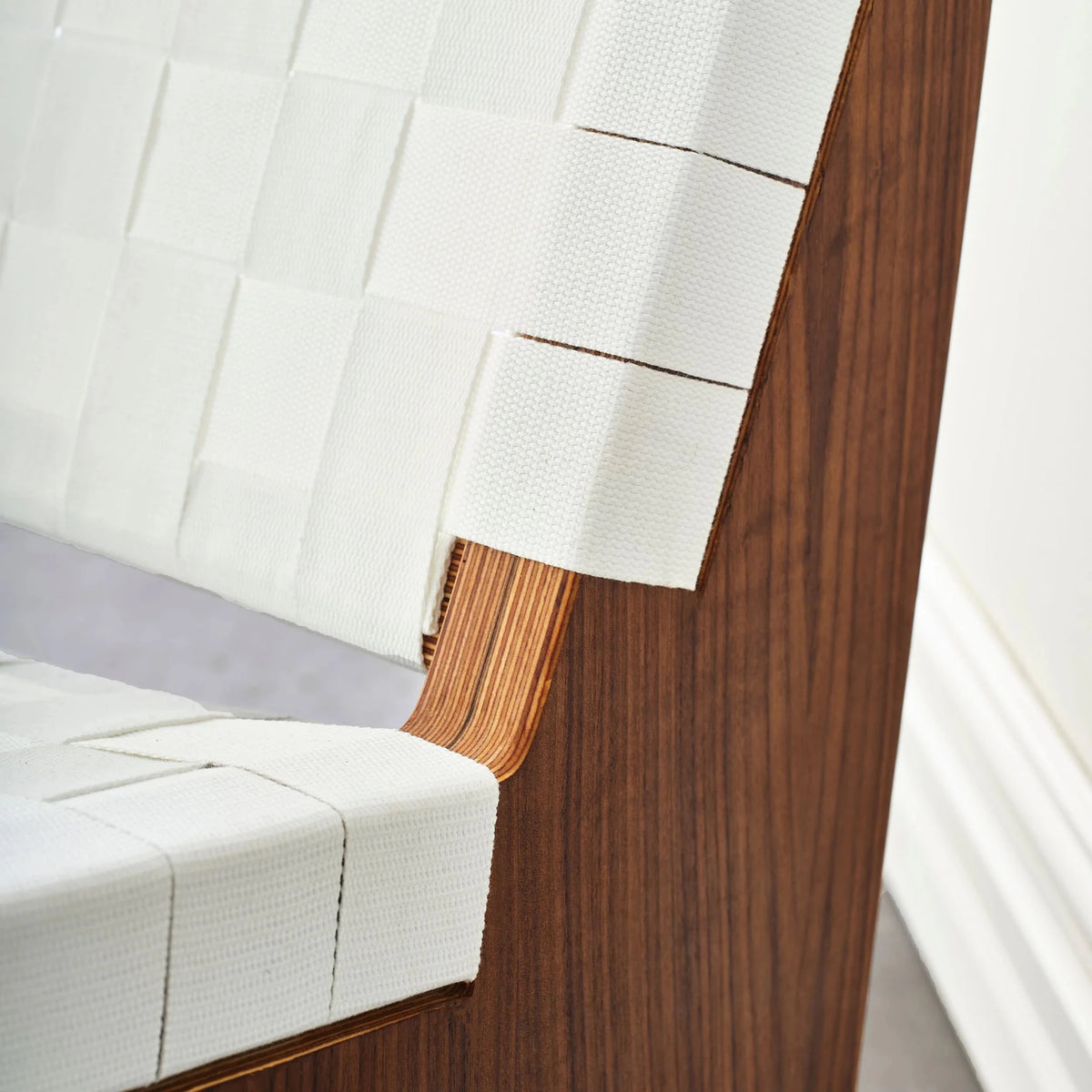 White woven fabric straps meeting walnut chair frame at seat-to-back junction closeup