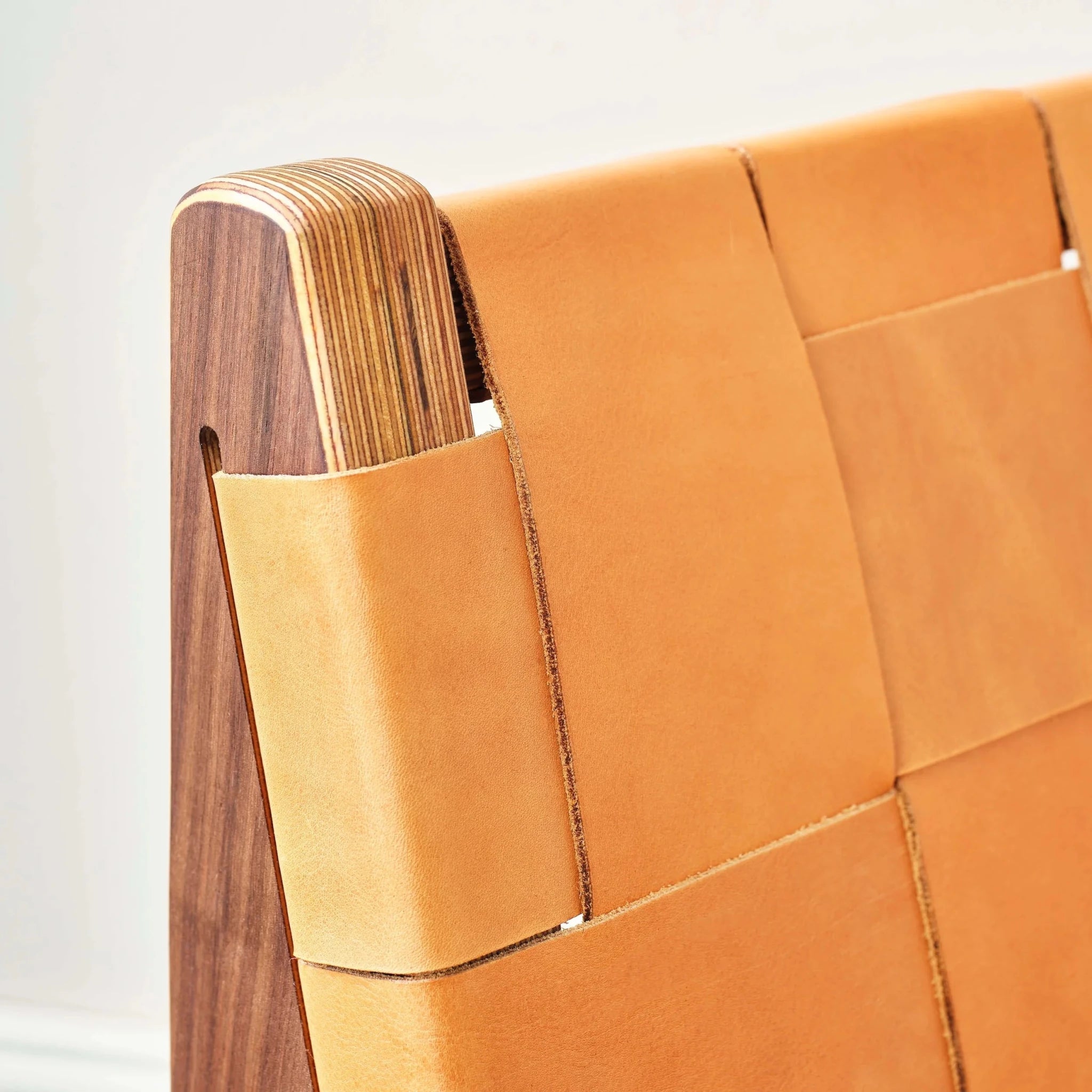 Close-up of chair backrest, tan woven leather straps over layered birch frame