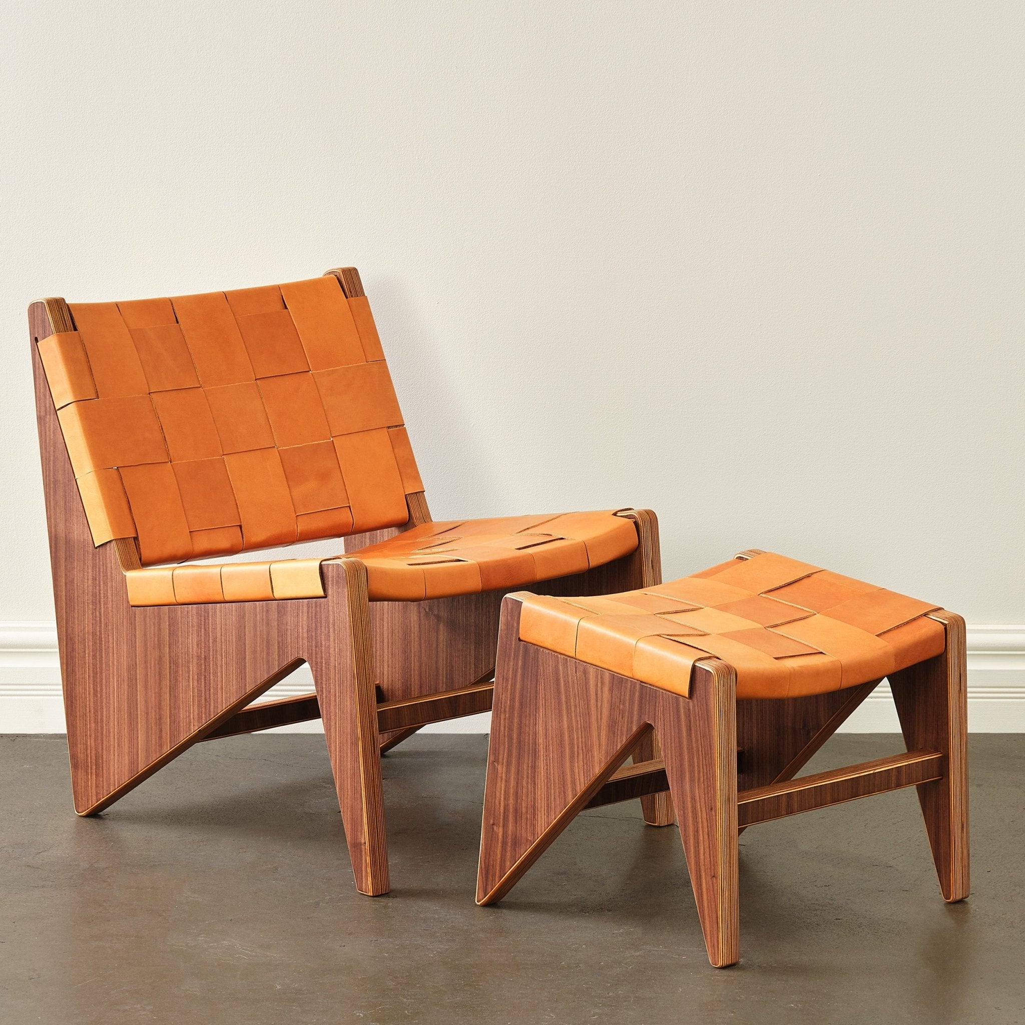 Walnut accent chair and ottoman with woven tan leather straps, front view, white wall