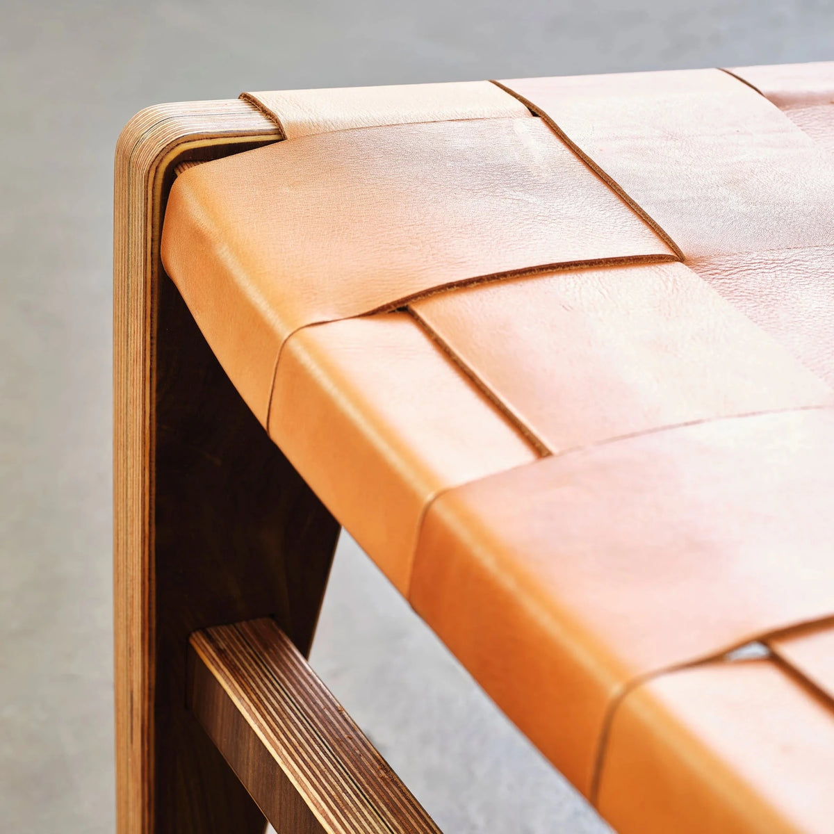 Extreme closeup of interwoven tan leather straps on walnut chair with birch edge
