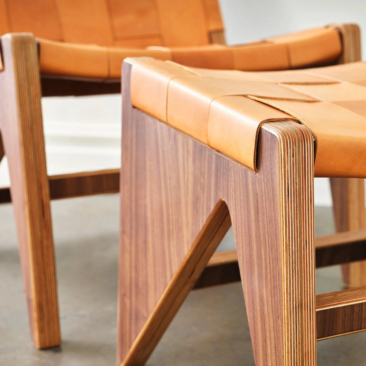 Closeup of walnut accent chair frame with woven tan leather seat and layered birch edges