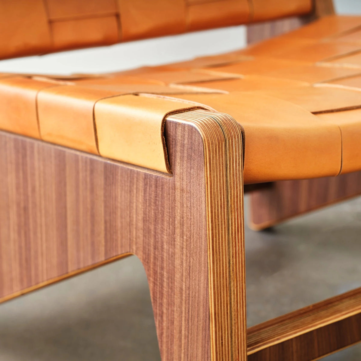Woven tan leather seat corner meeting walnut leg with exposed layered birch plywood edge