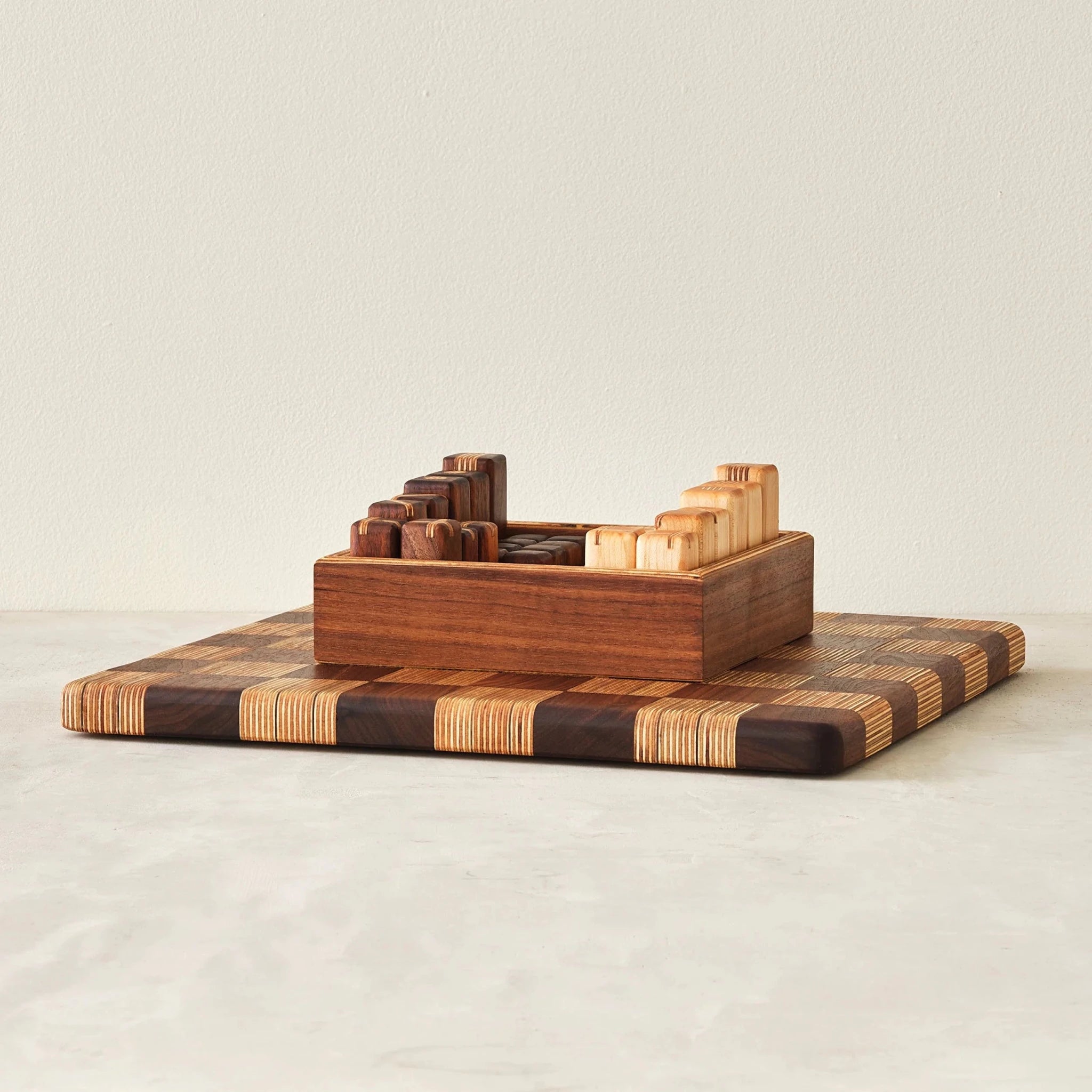 Walnut storage box of game pieces resting on striped checkerboard board, angled view