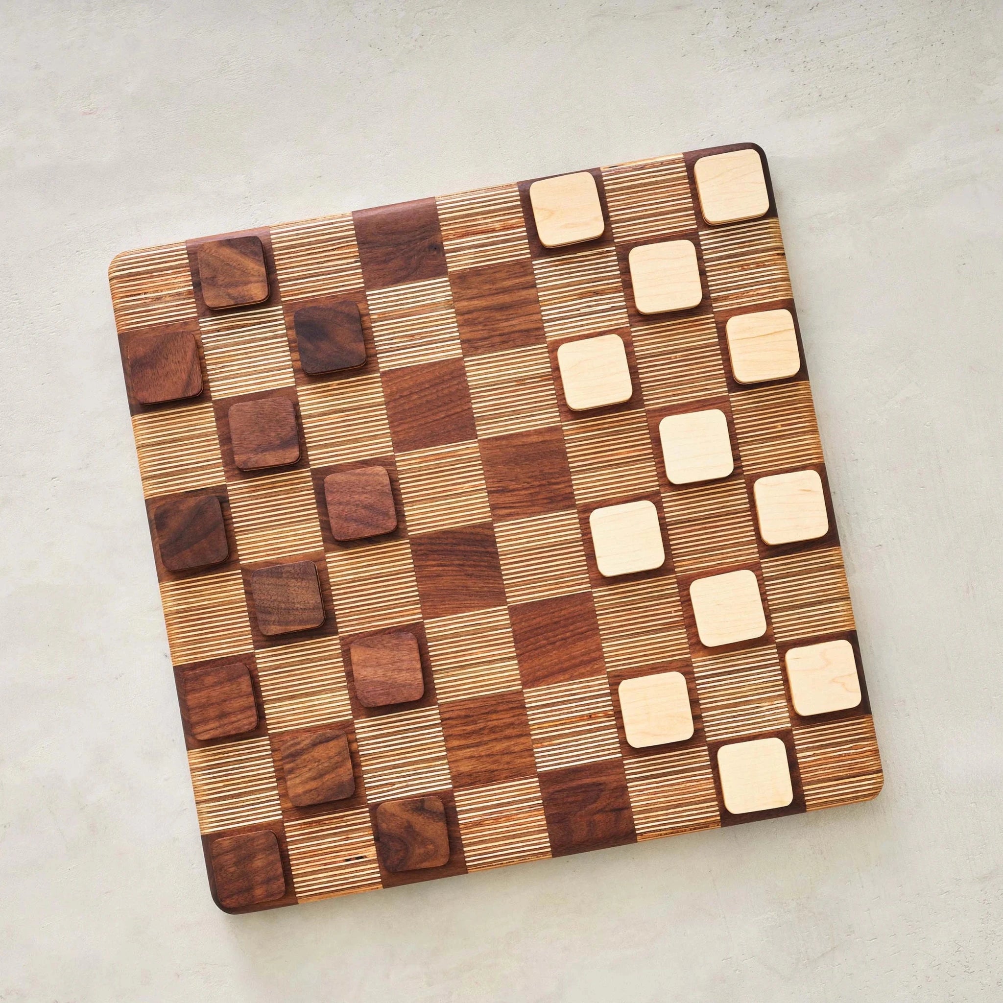 Overhead view of walnut and maple checkers discs set up on opposite board sides