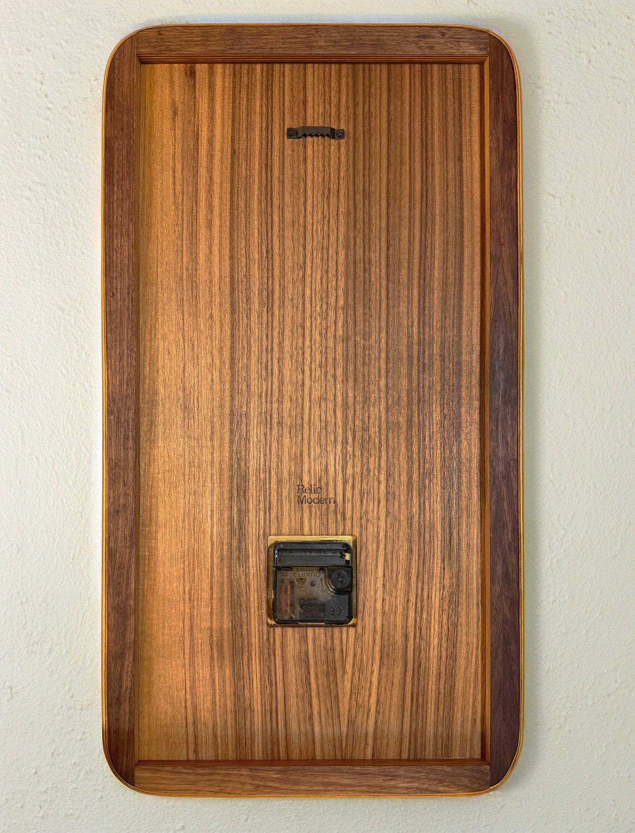Backside of a walnut wooden clock showing the mechanism and hanger, brand logo that says Relic Modern.
