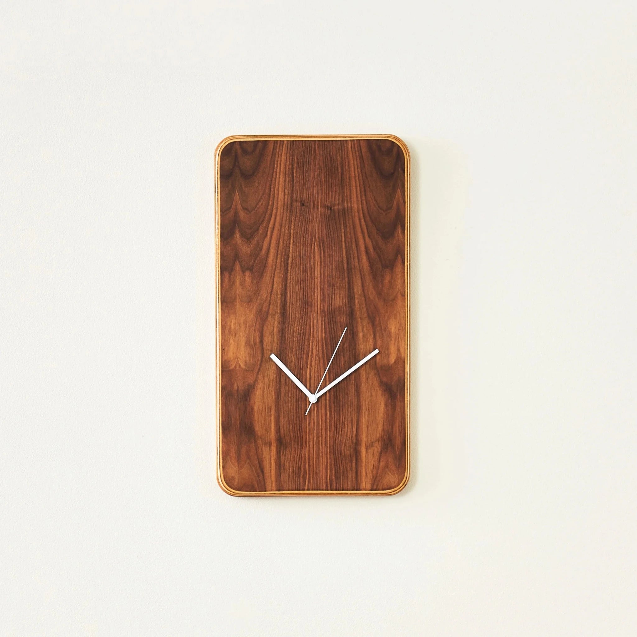 Vertical walnut wall clock with minimalist white hands on off-white wall