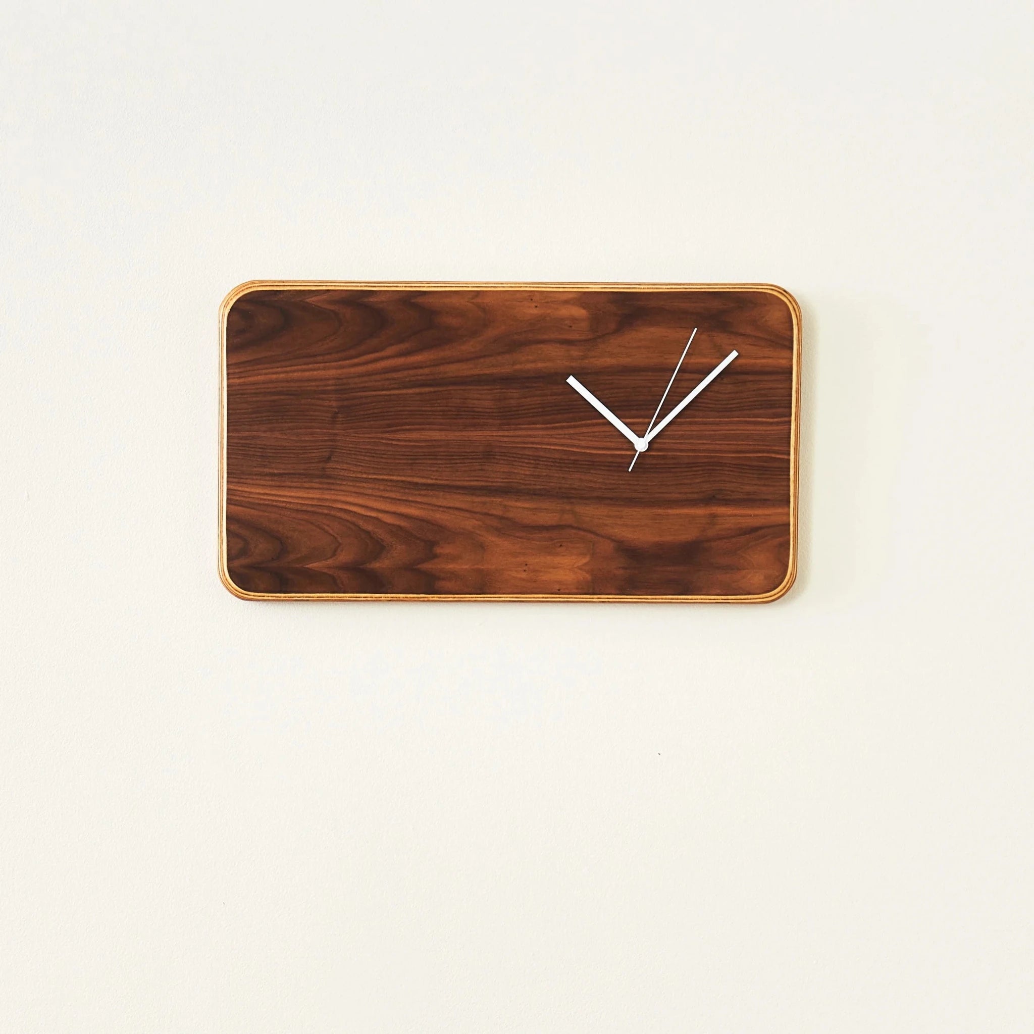 Horizontal walnut wall clock with white hands mounted on cream wall