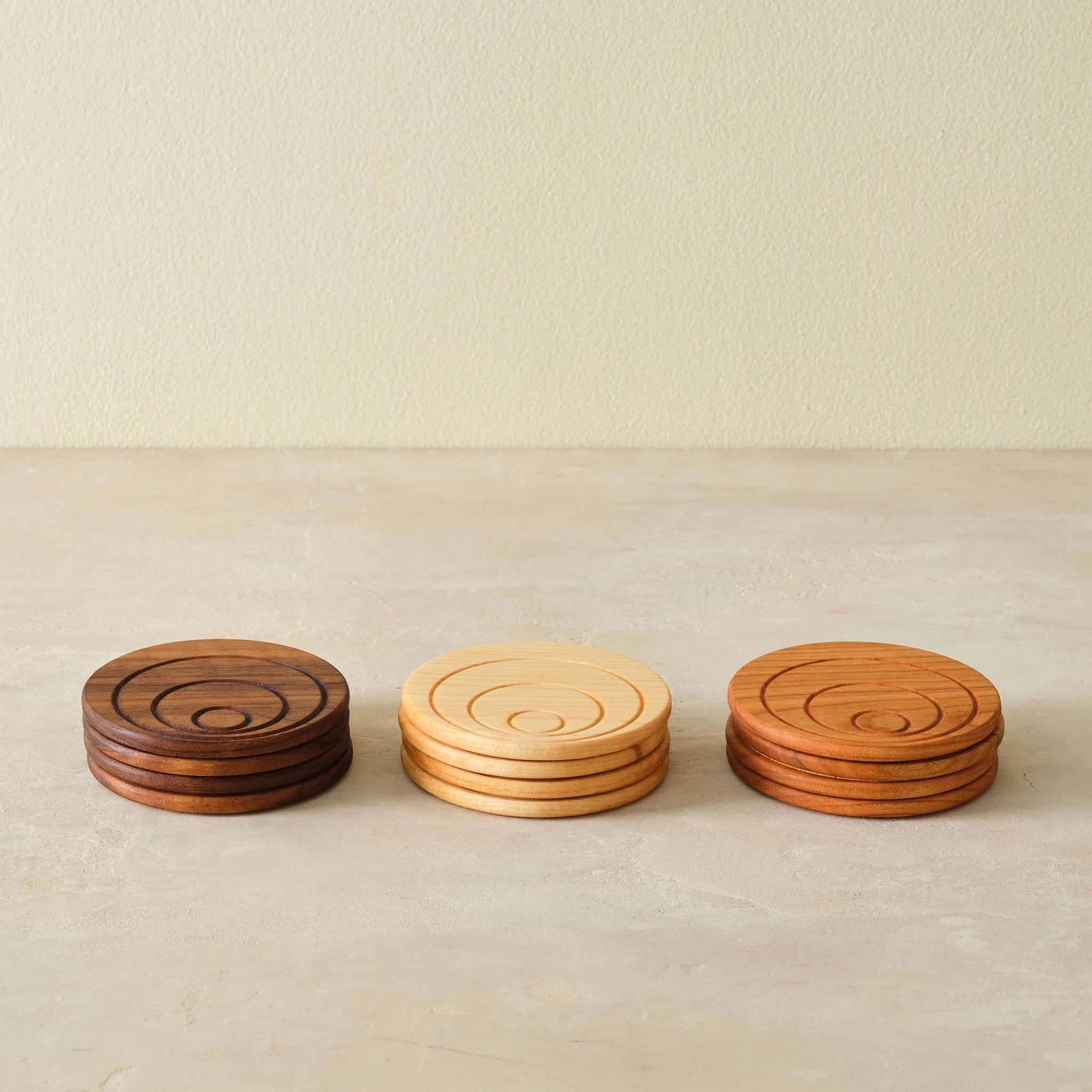 Three stacked coaster sets—walnut, maple, cherry—front view on countertop