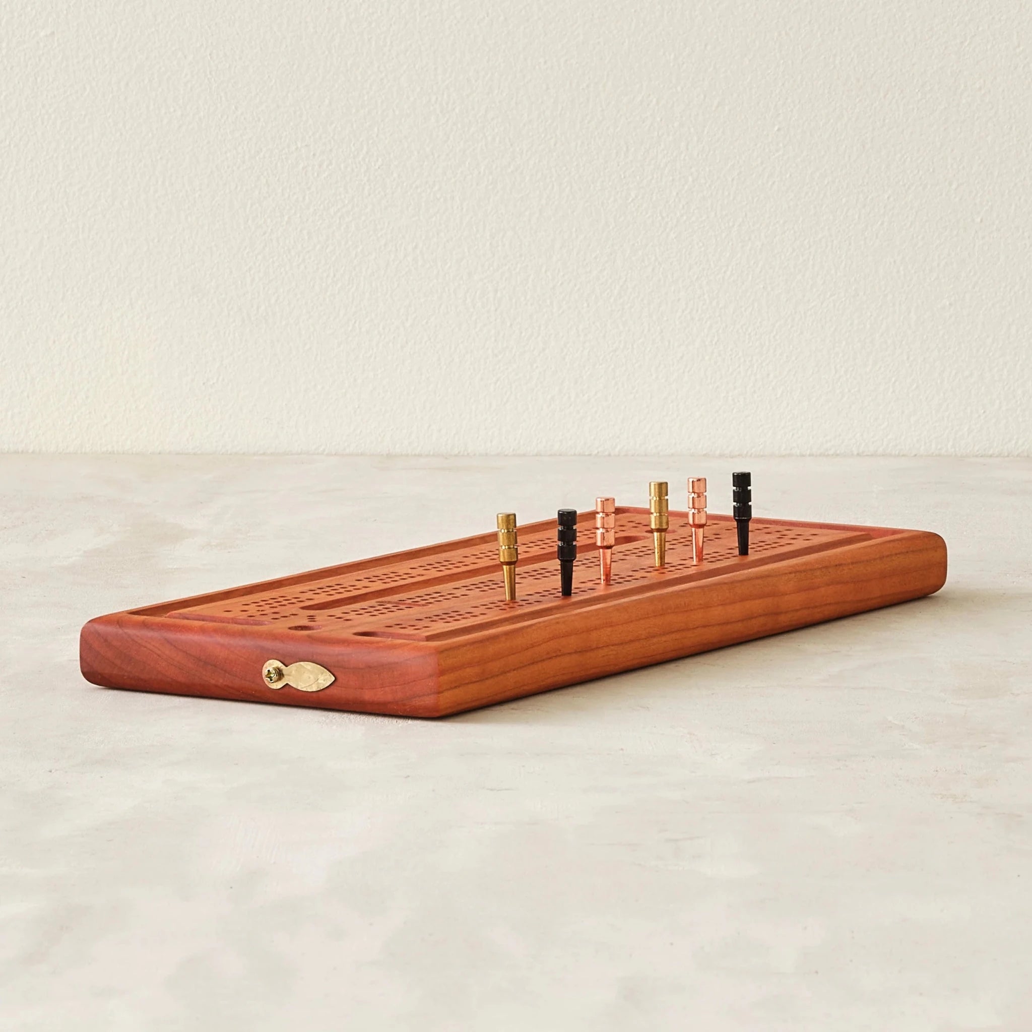 Cherry cribbage board angled view with brass, copper, black pegs standing upright