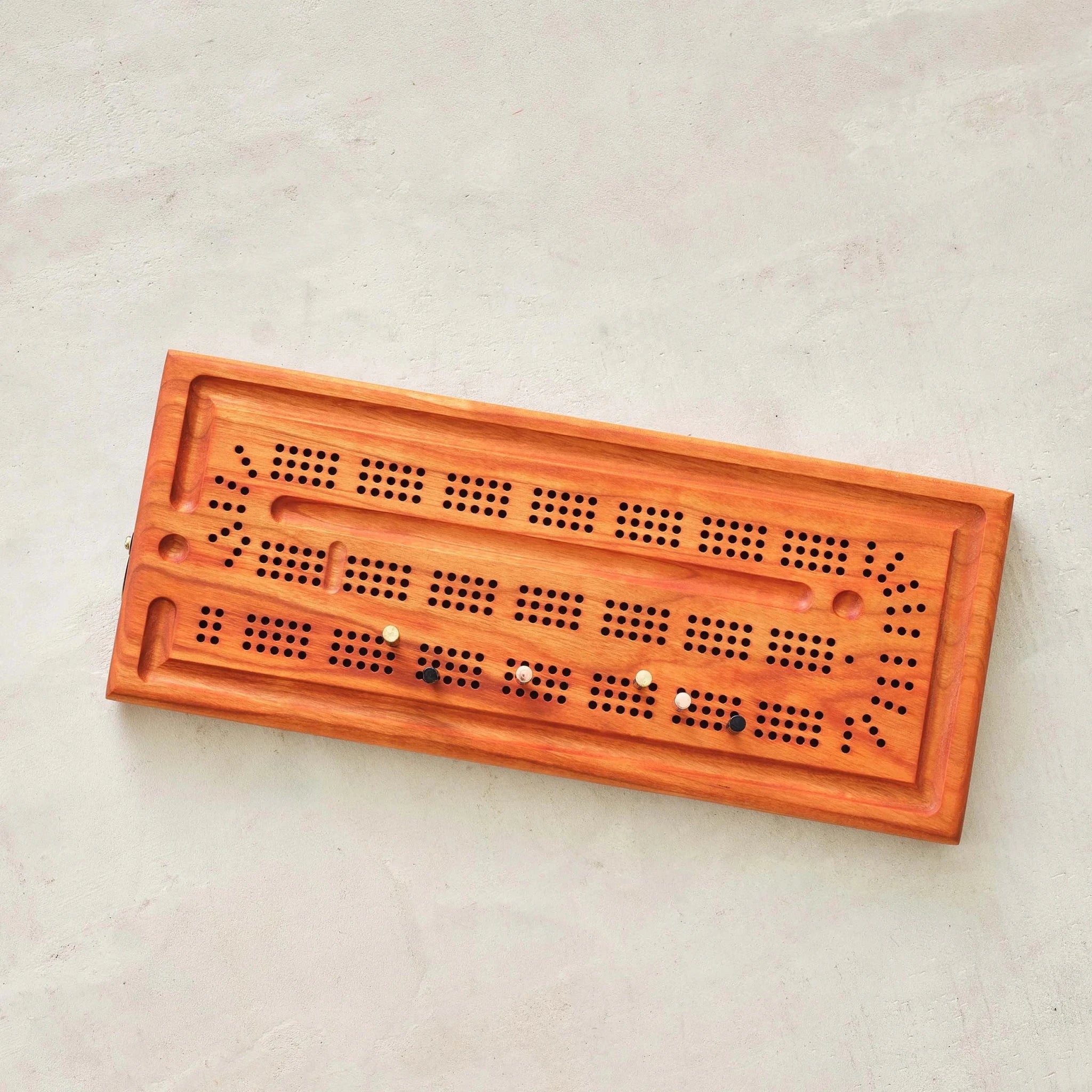 Cherry cribbage board top view, reddish grain, colored pegs on concrete surface
