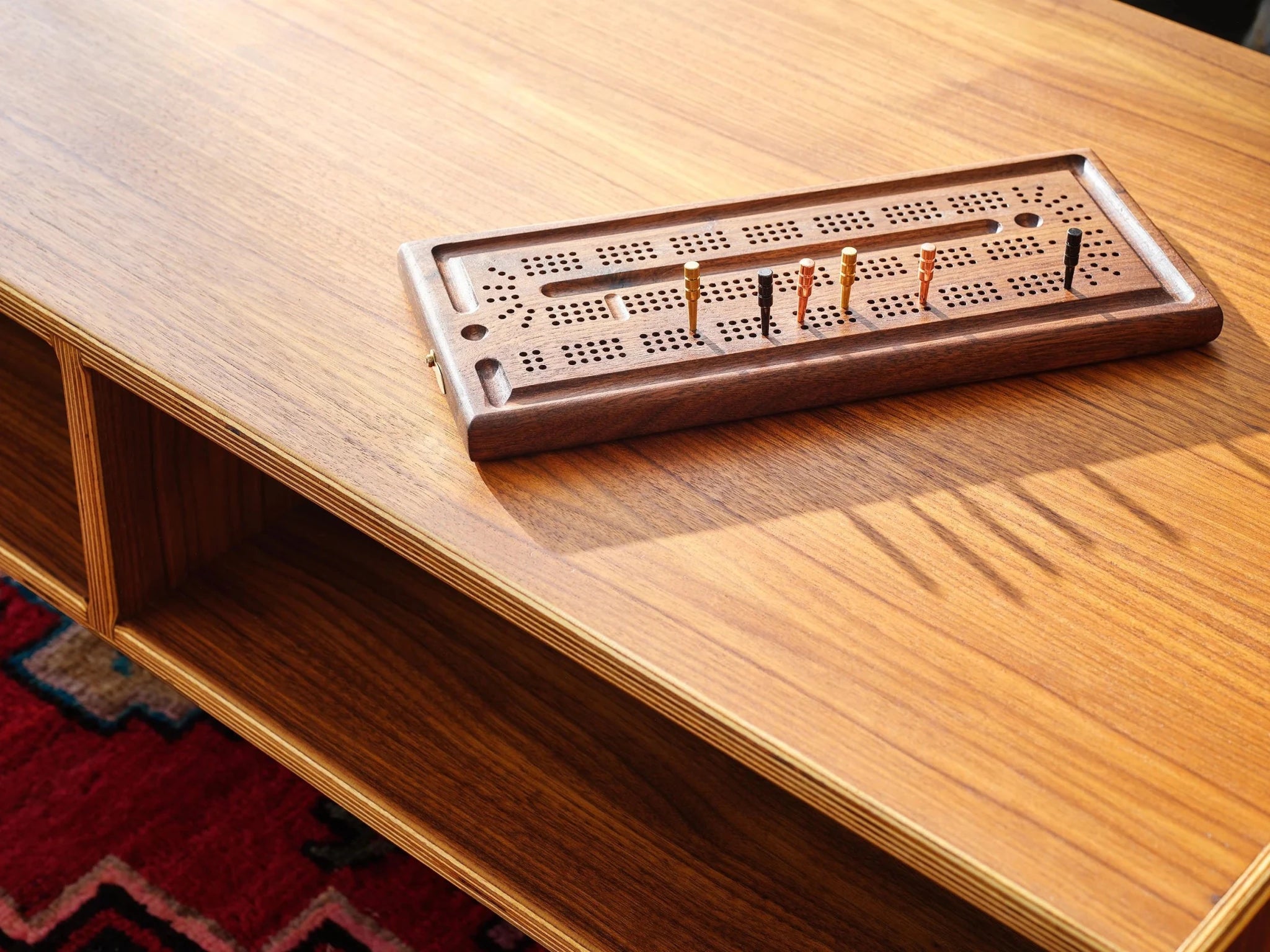 Walnut cribbage board with pegs on walnut coffee table, red rug below