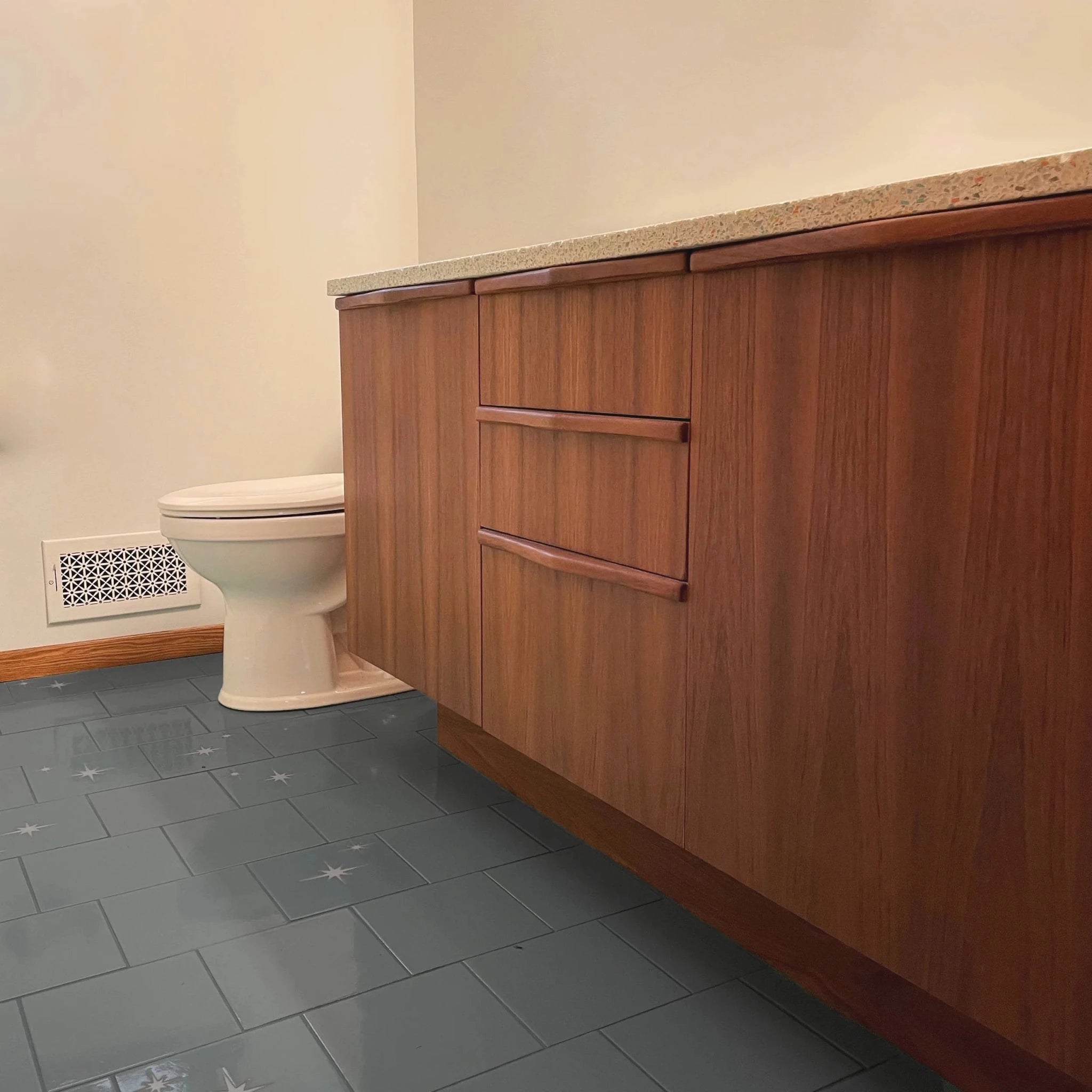 Angled side view of long teak vanity, terrazzo top, wood pulls, gray tile