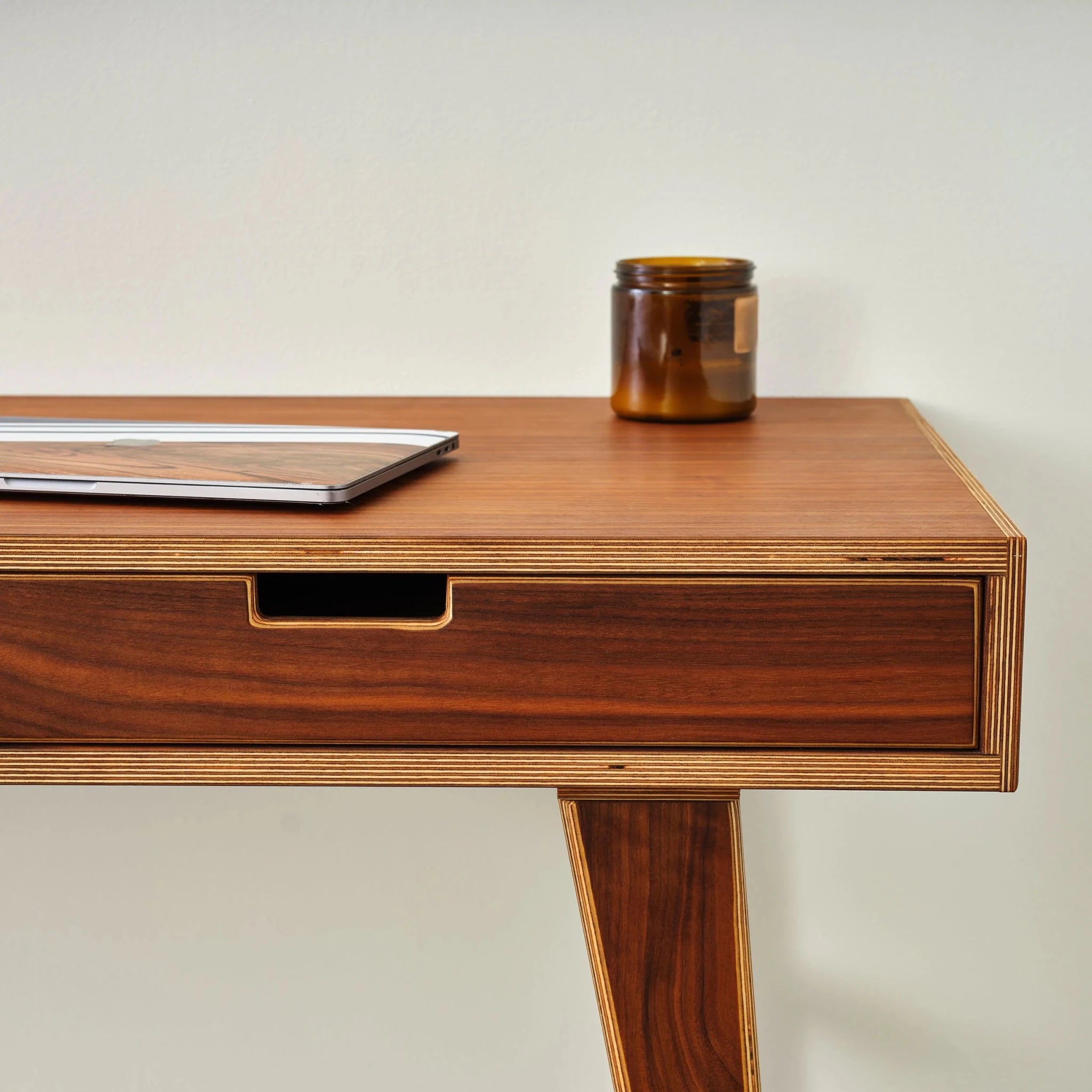 Walnut writing desk corner closeup, single drawer, laptop and amber candle jar on top