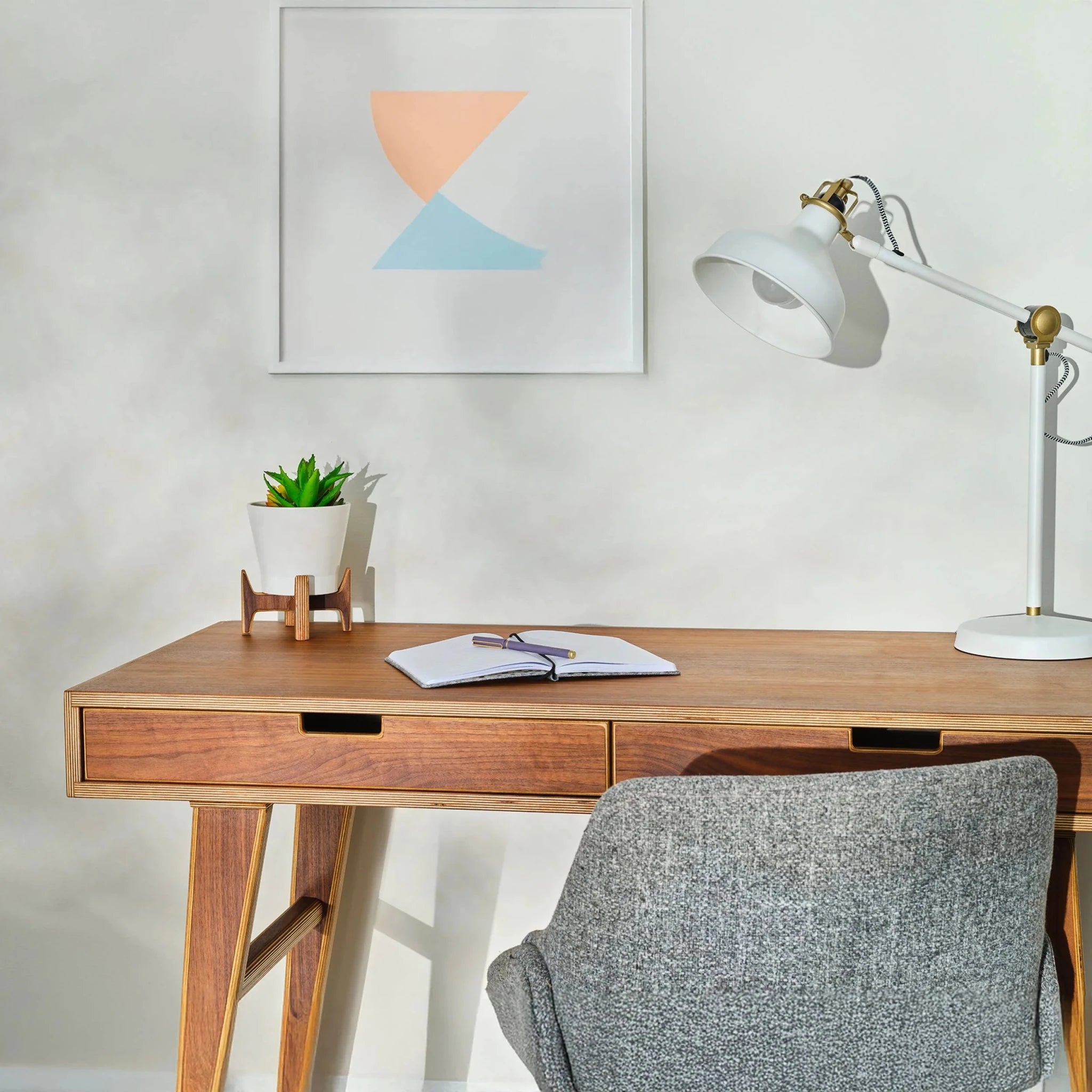 Walnut writing desk styled in office with lamp, plant, framed art, gray chair