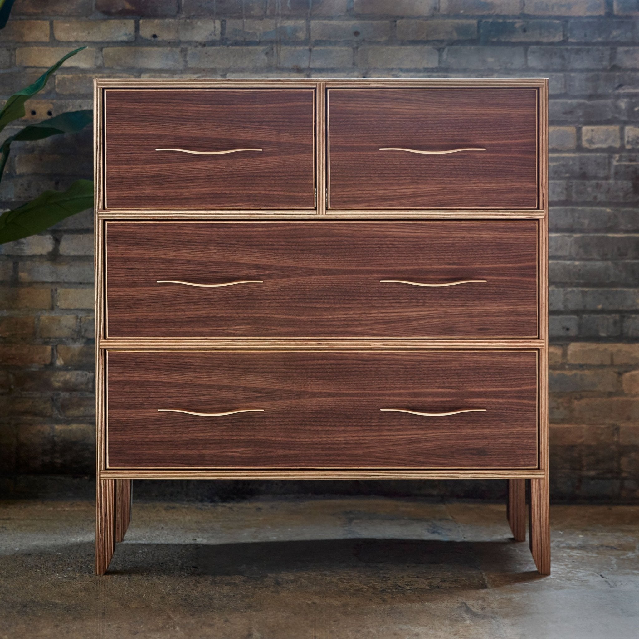 Walnut dresser front against exposed brick wall, closed drawers, plant at left
