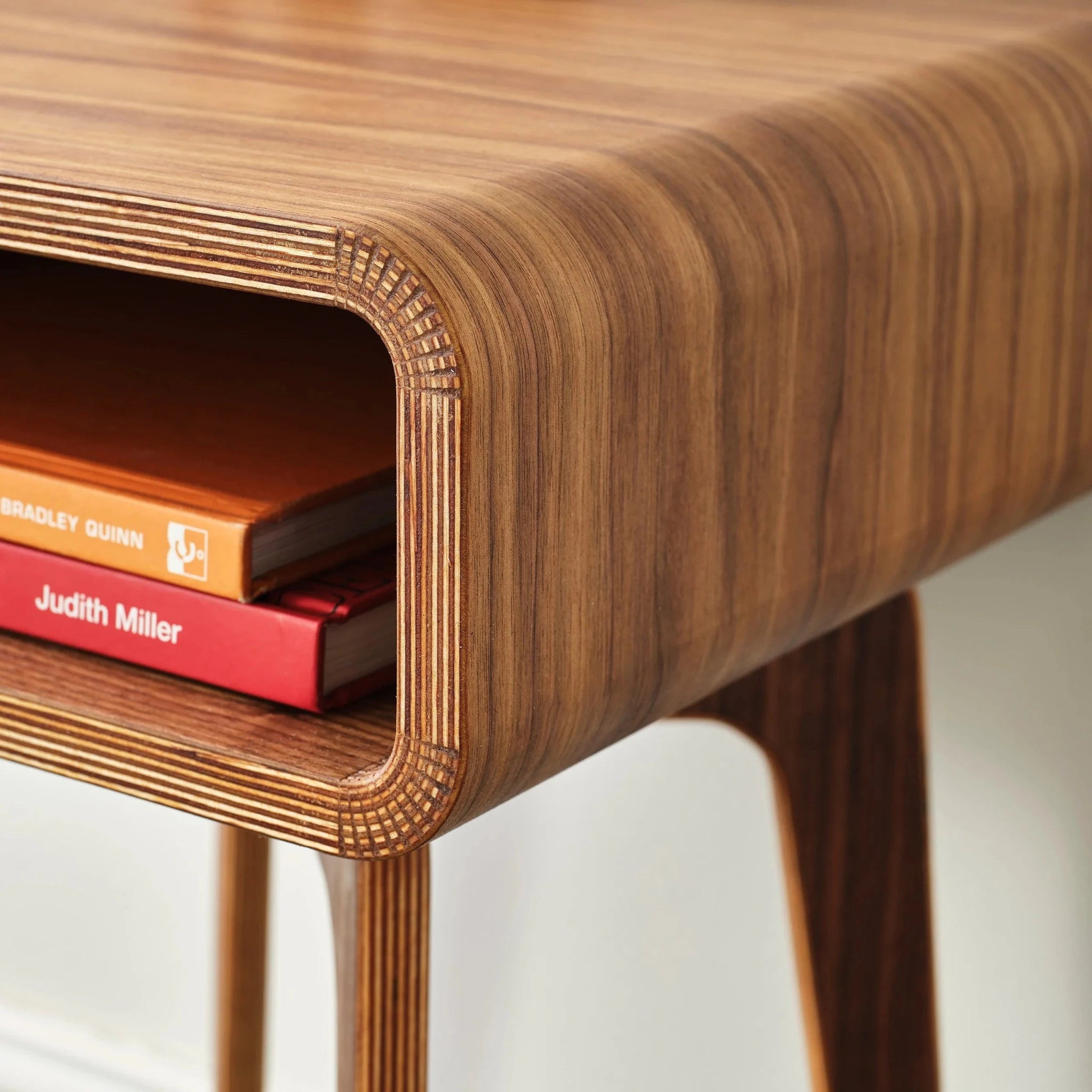 Close-up walnut end table cubby holding orange and red mid-century books, ply edge