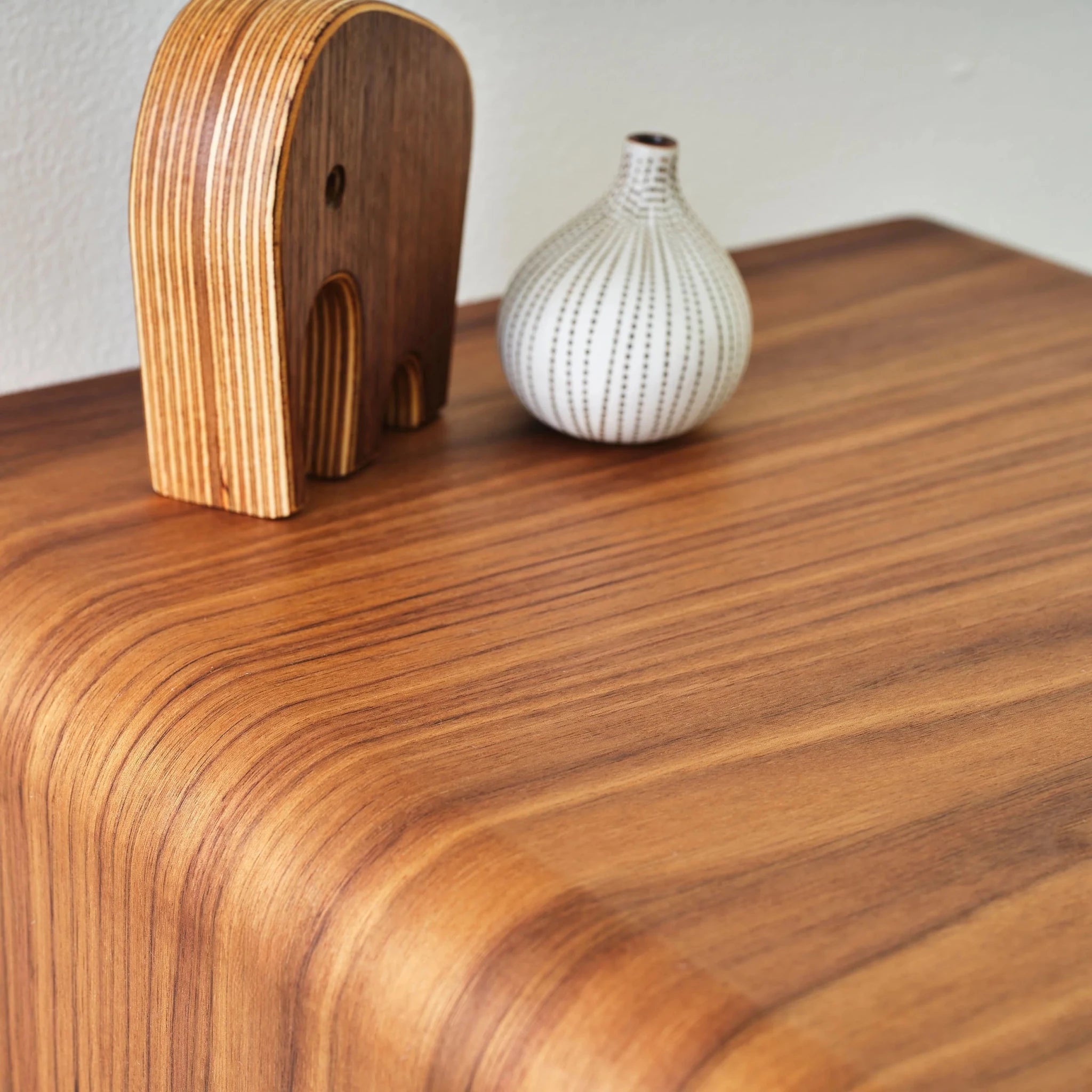 Walnut end table top surface with wooden elephant figure and striped white vase