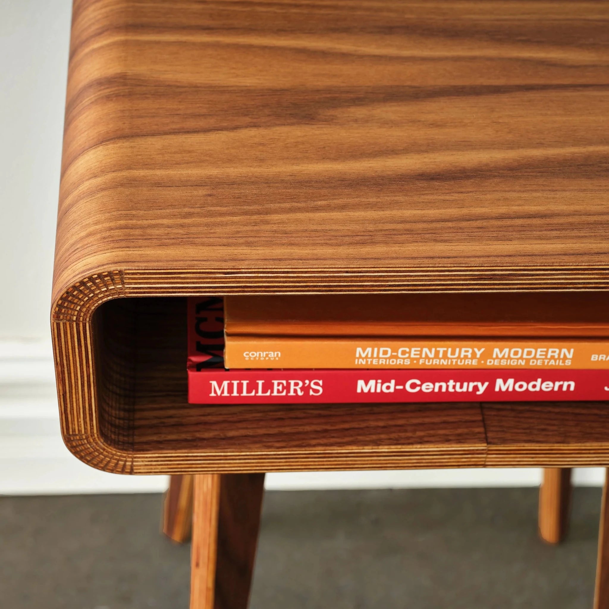 Overhead close-up of walnut end table top, curved edge, books in cubby