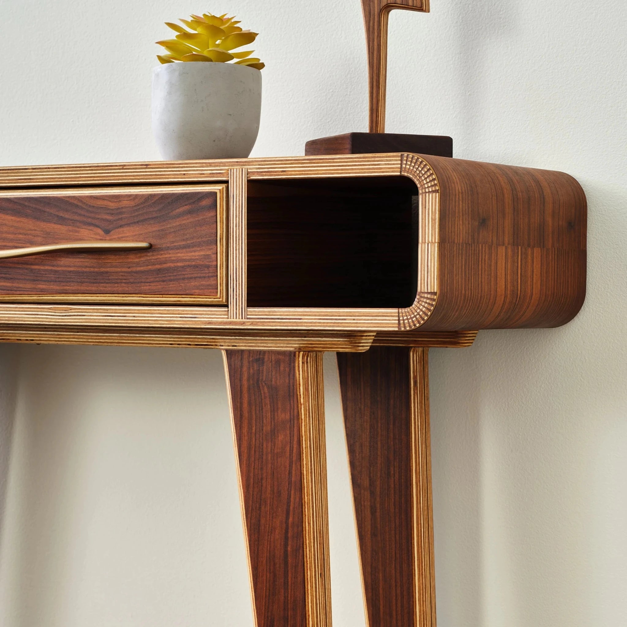 Angled close-up of walnut entry table, layered birch edges, open cubby, succulent and sculpture